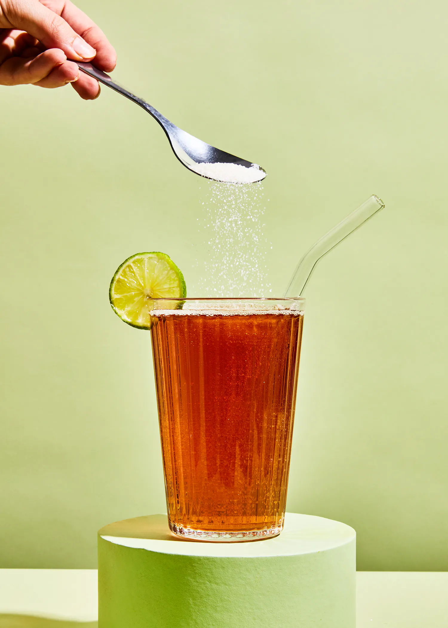 eine Person gießt Zucker in ein Glas Tee