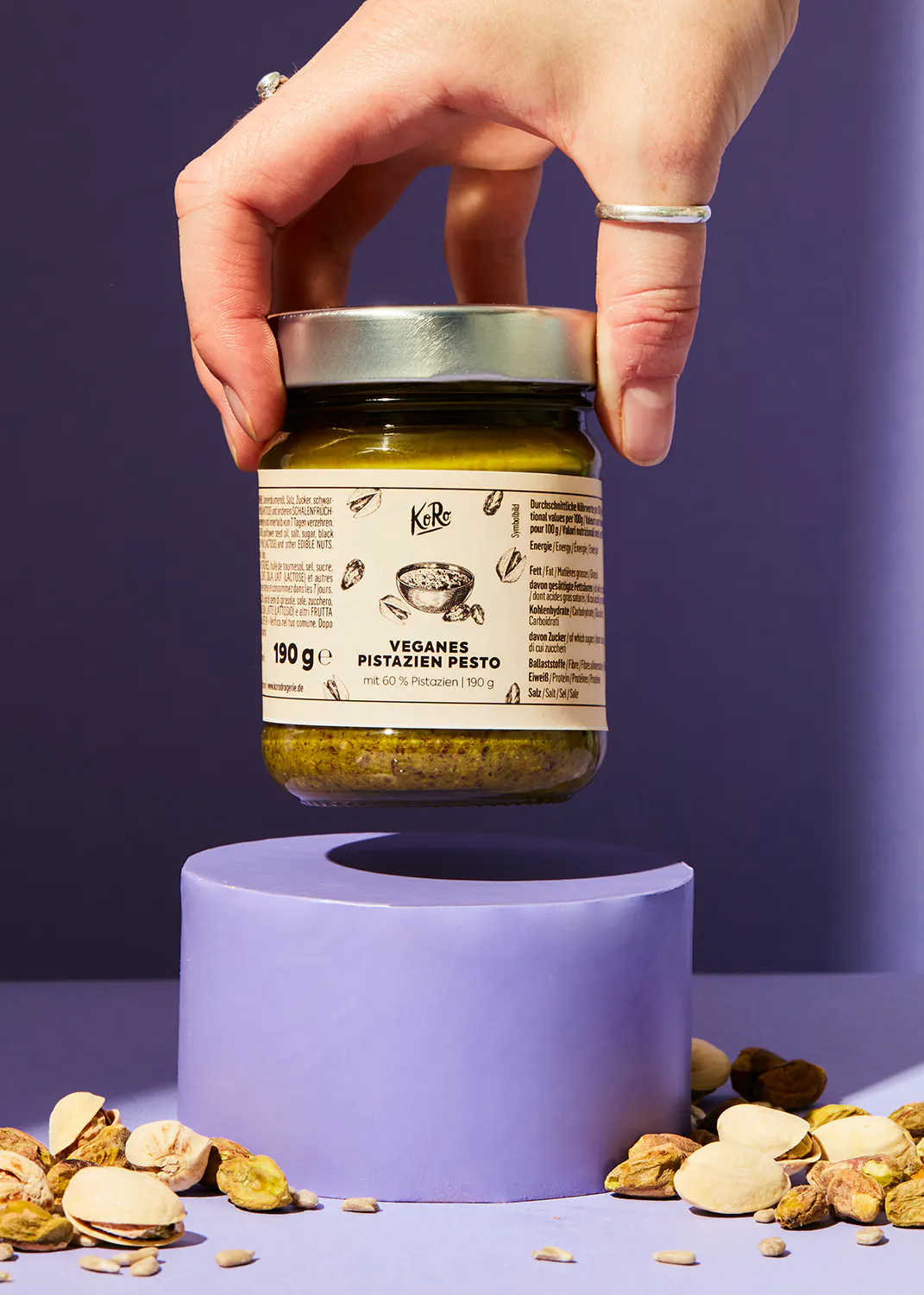 une personne tient un bocal de pesto végétalien à côté de pistaches