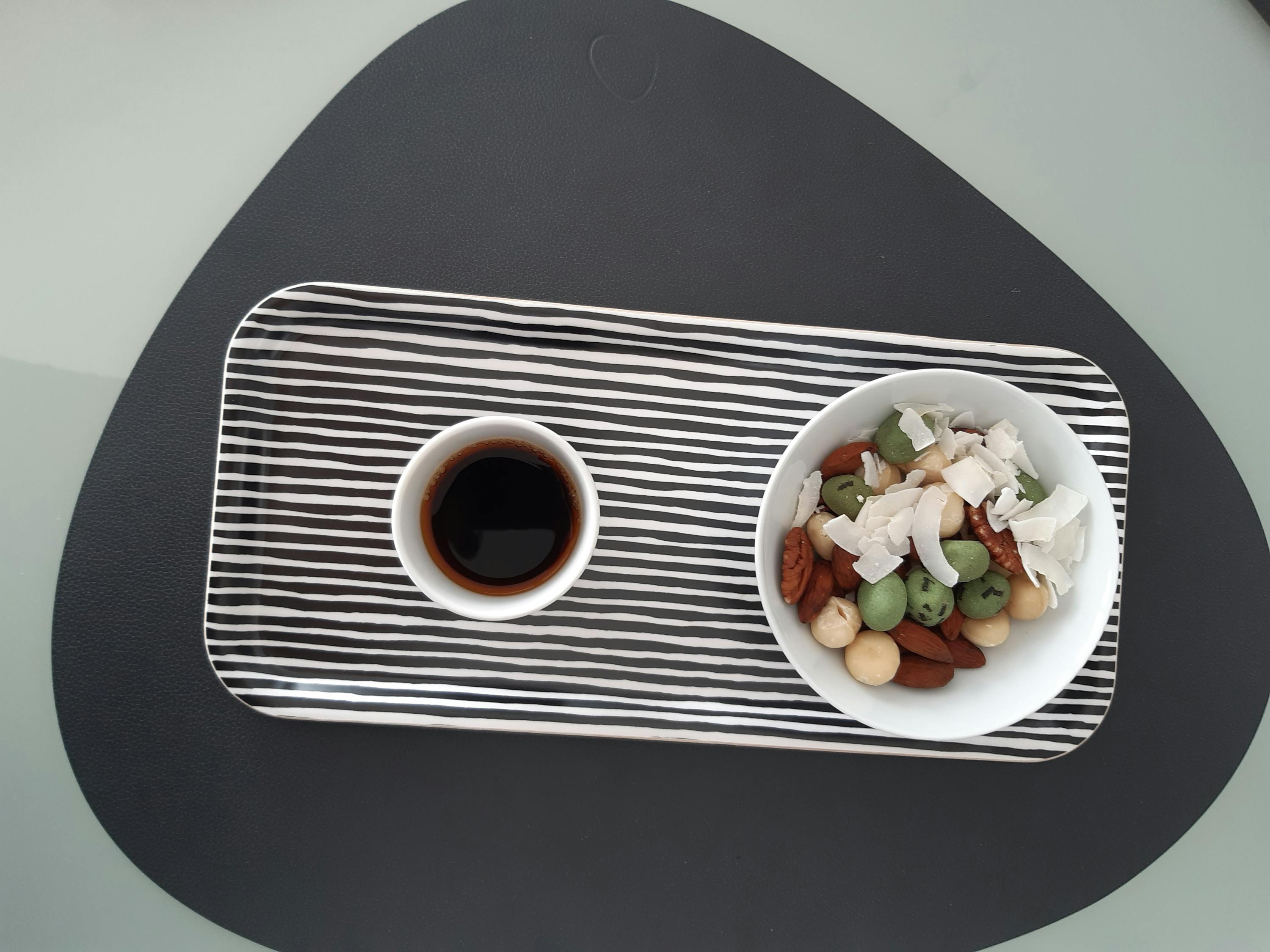 ein Tablett mit einer Tasse Kaffee und einer Schüssel Nüsse