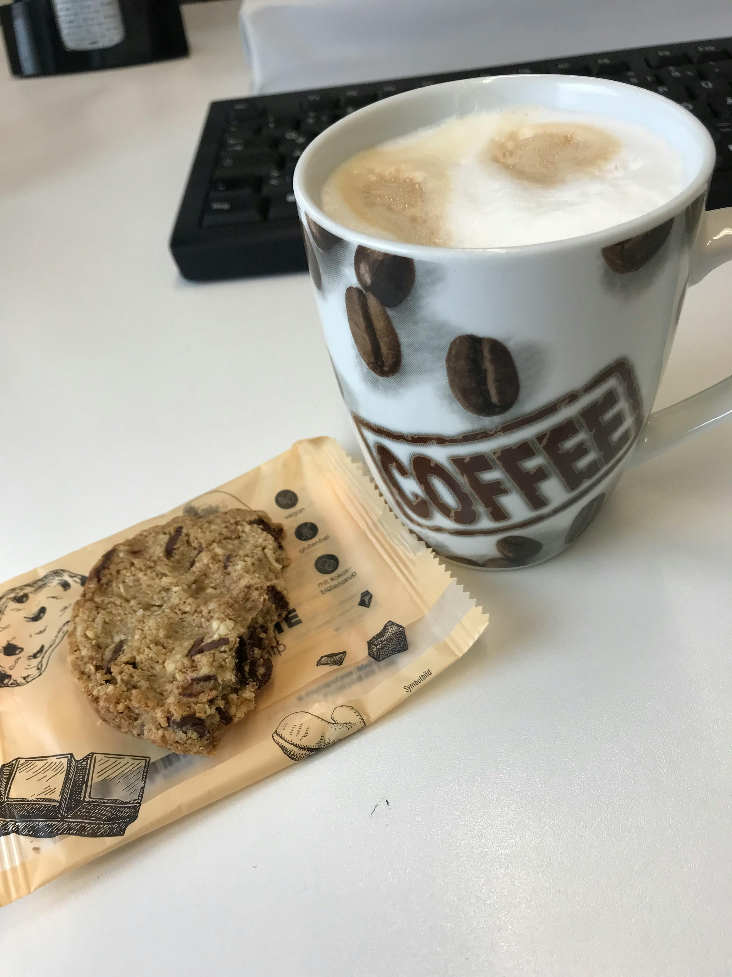a mug that says coffee on it next to a cookie