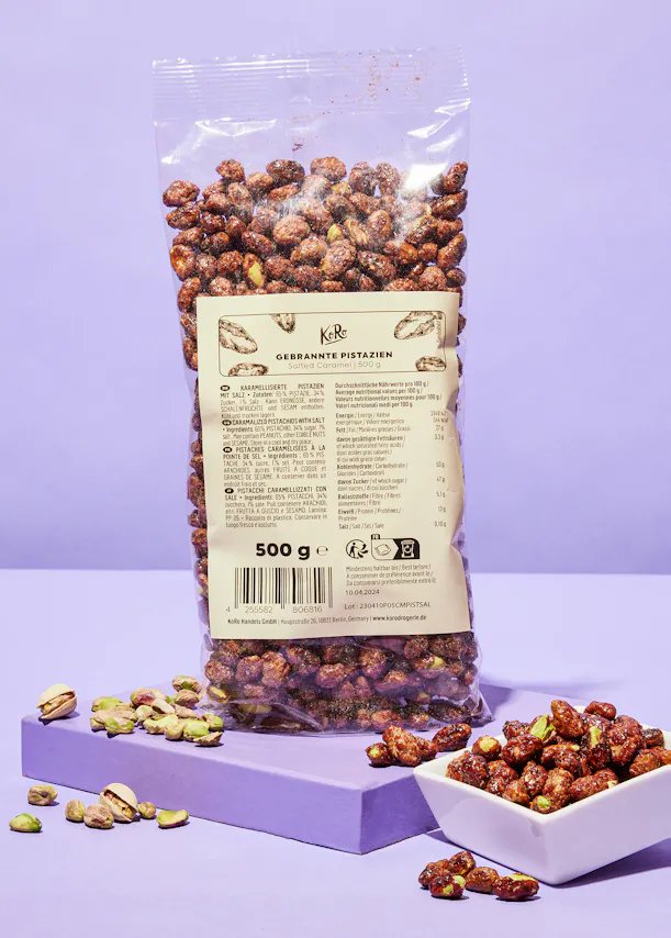 un sac de pistaches est sur une table violette à côté d' un bol de pistaches