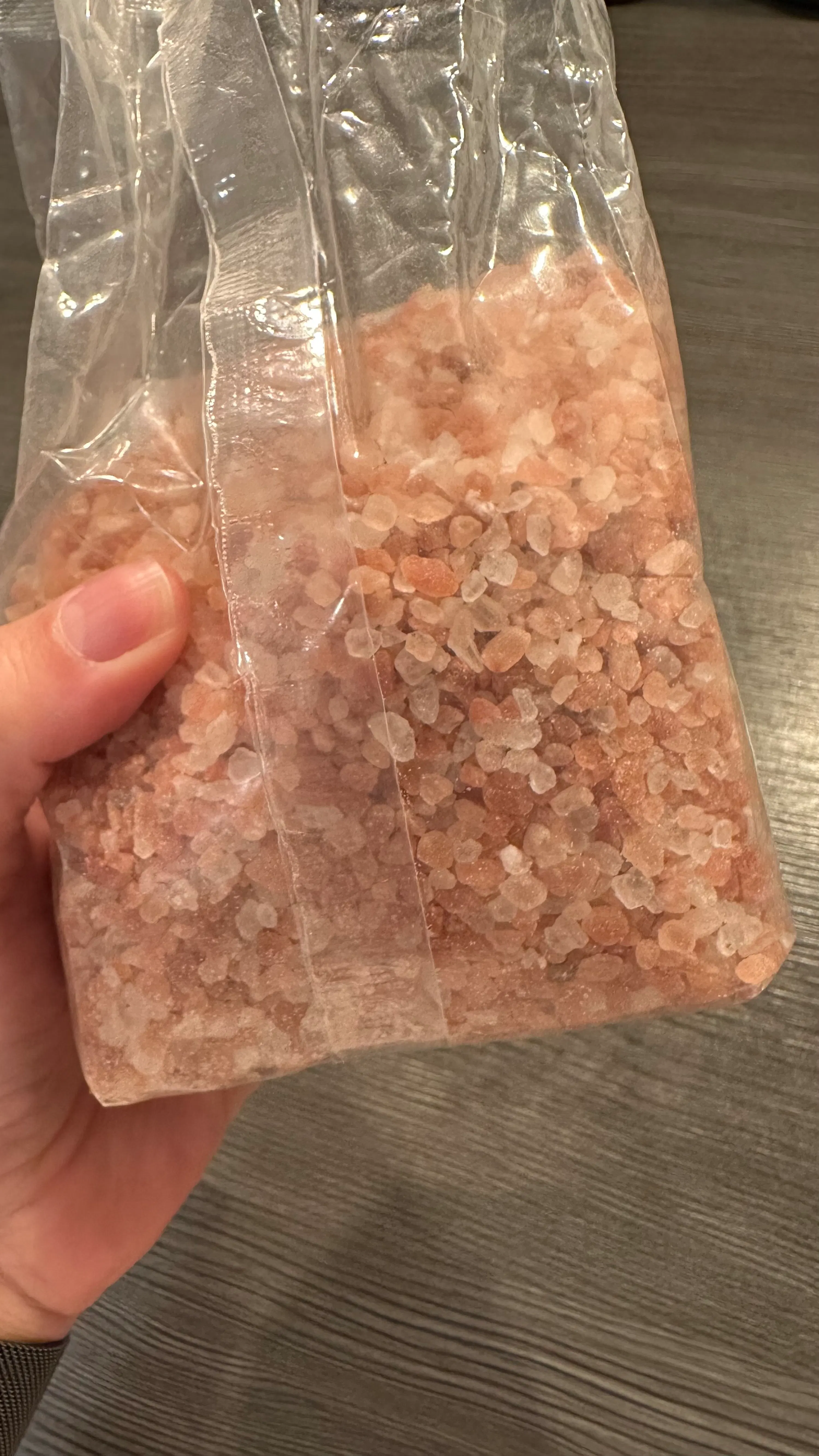 une main tient un sac en plastique transparent rempli de gros sel rose de l'himalaya.