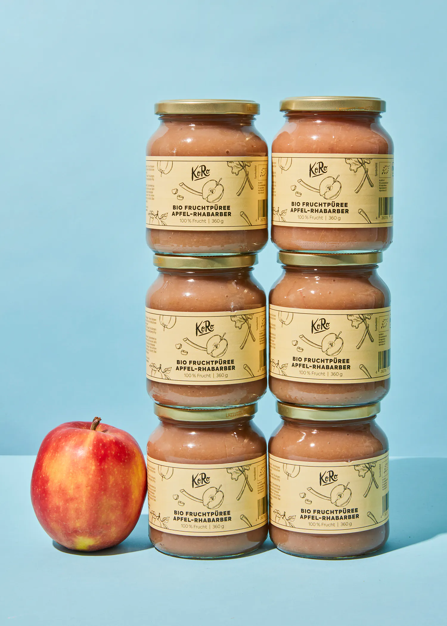 sechs Gläser fruchtpüree stehen neben einem roten Apfel