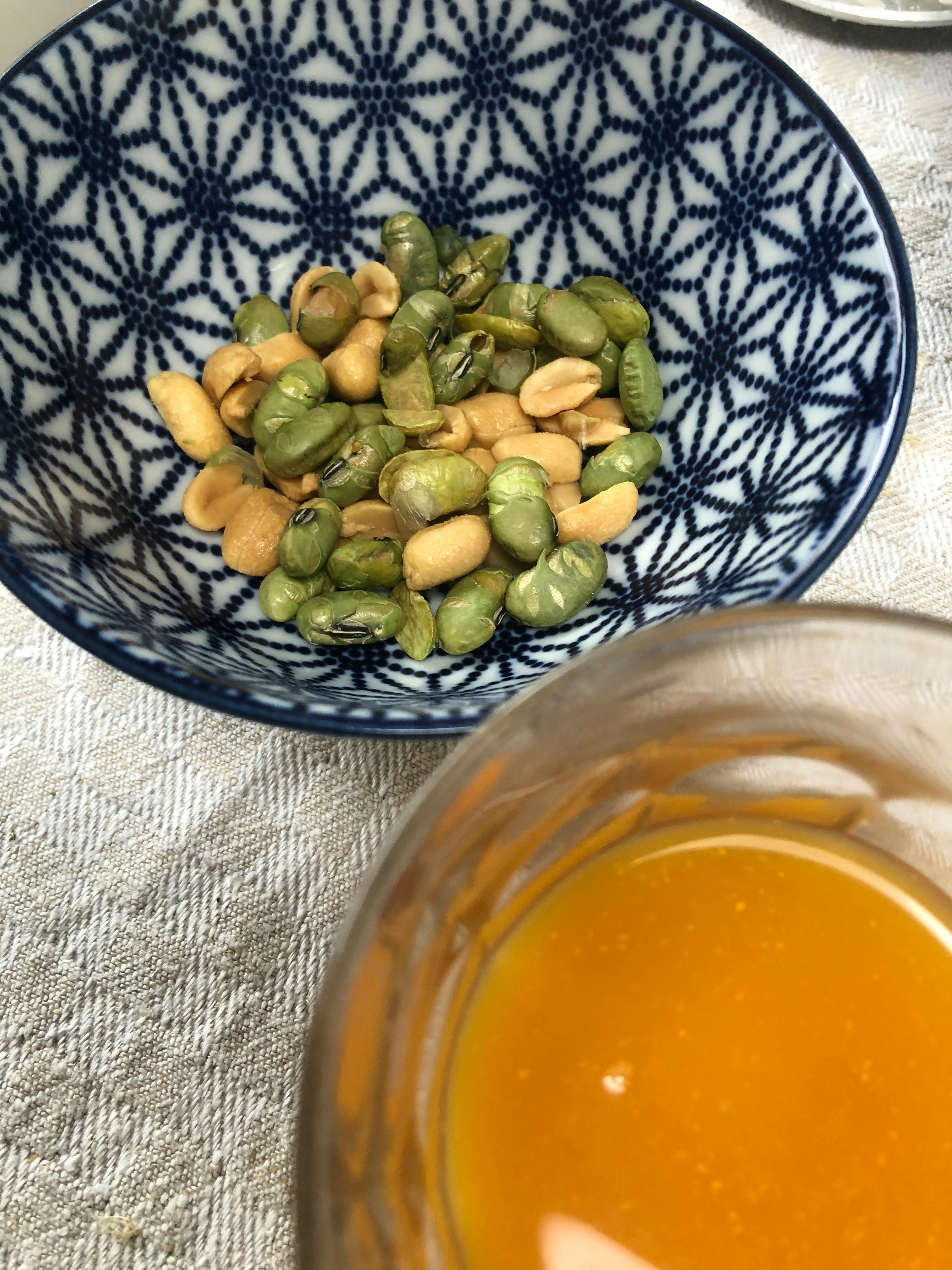 una ciotola di arachidi e fagioli verdi accanto a un bicchiere di salsa