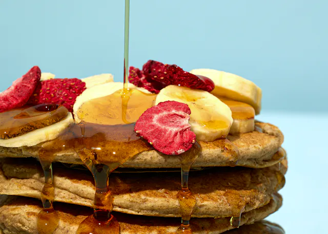 une pile de crêpes avec des fraises séchées et des bananes sur le dessus