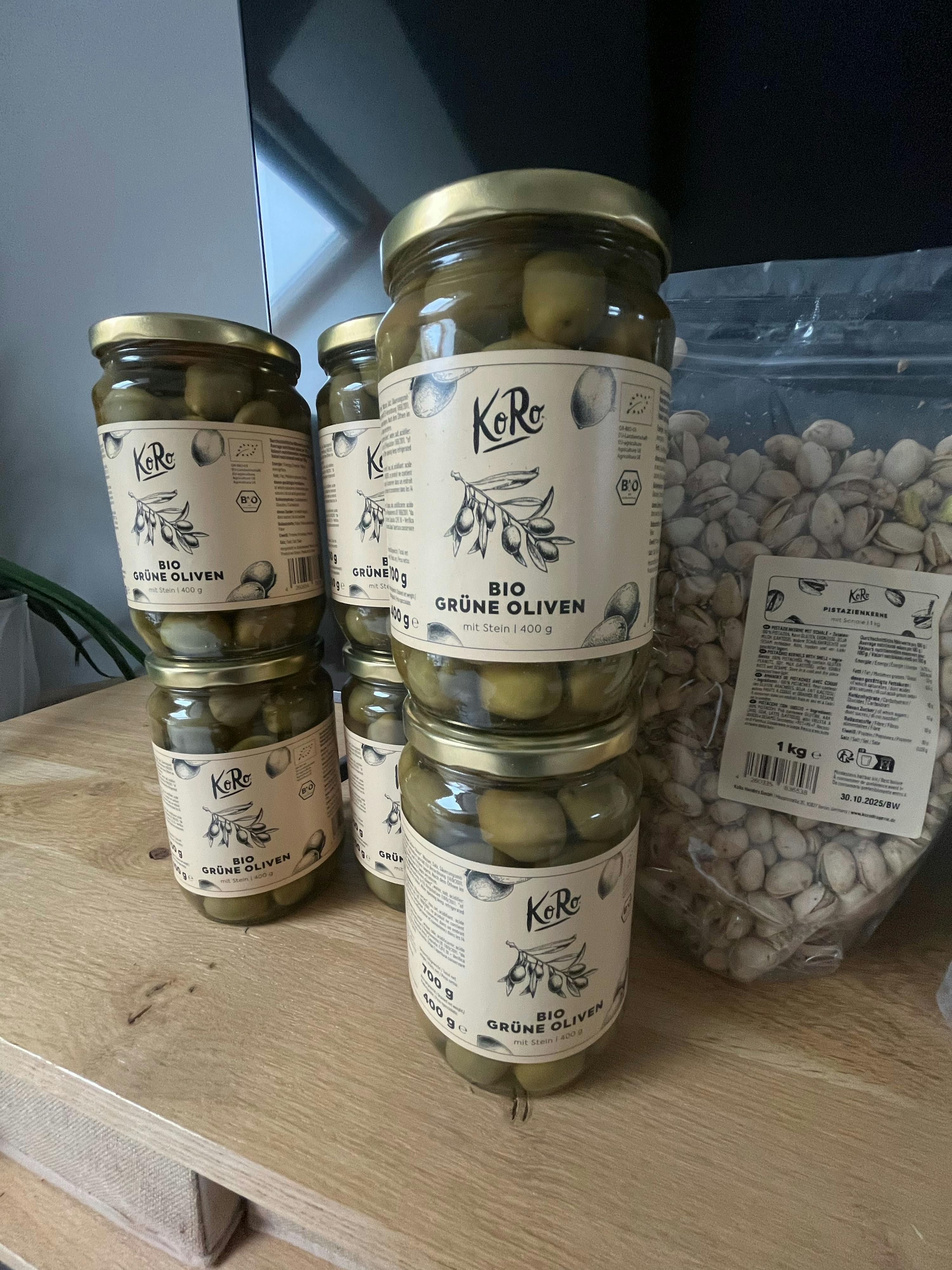 sechs Gläser grüner Oliven stehen auf einem Holztisch