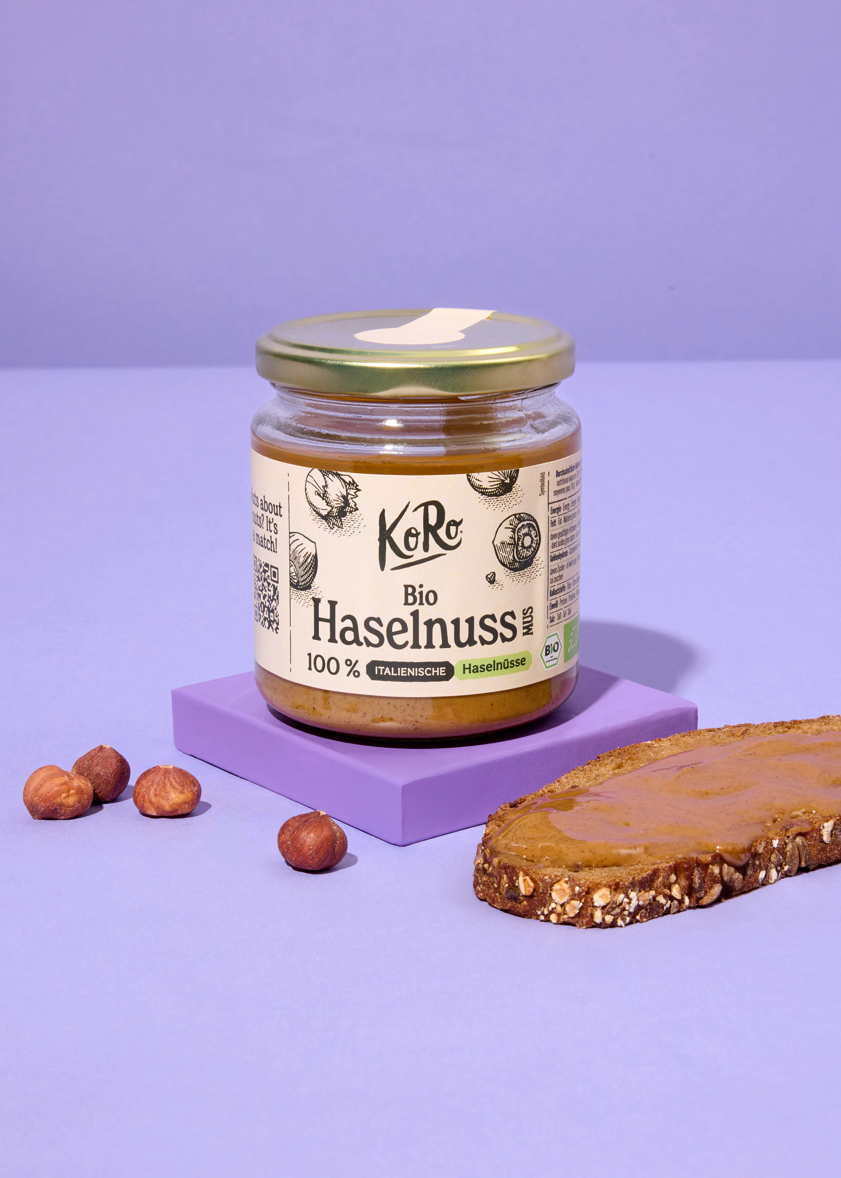 un bocal d' hazelnuss bio est assis sur une table violette à côté d' une tranche de pain
