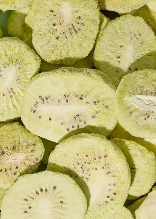 a close-up of many dried kiwi slices showing their light green color and dark seeds.