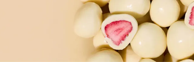 white chocolate-covered strawberries, with one cut in half to reveal a bright pink dried strawberry inside.