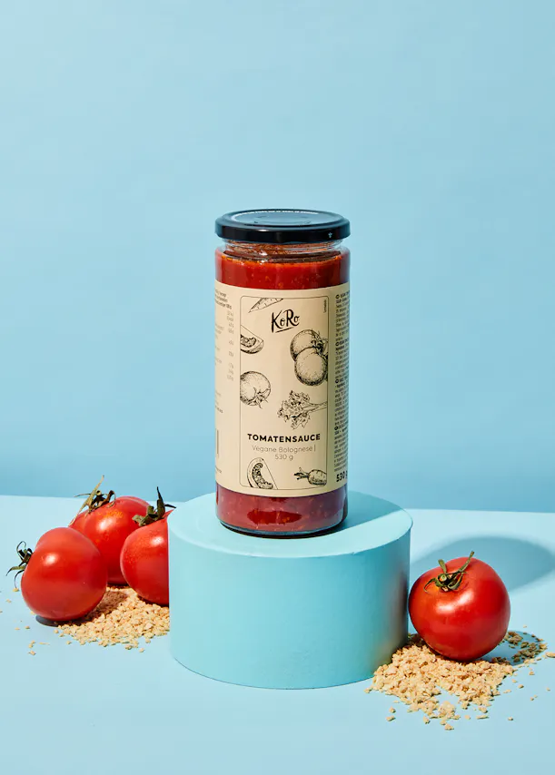 un bocal de sauce tomate est posé sur un support bleu entouré de tomates