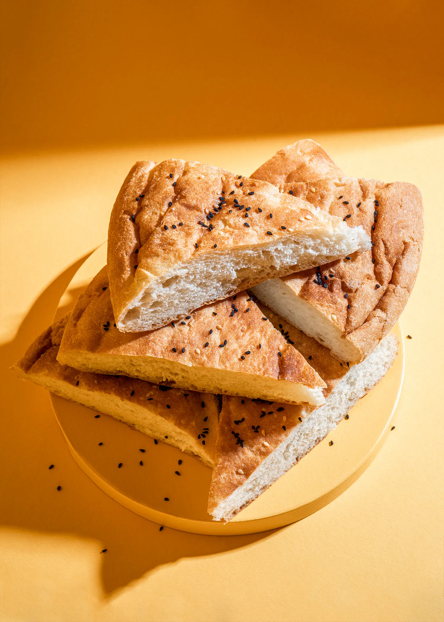 ein Stück Brot mit schwarzen Sesamkörnern auf einem gelben Teller