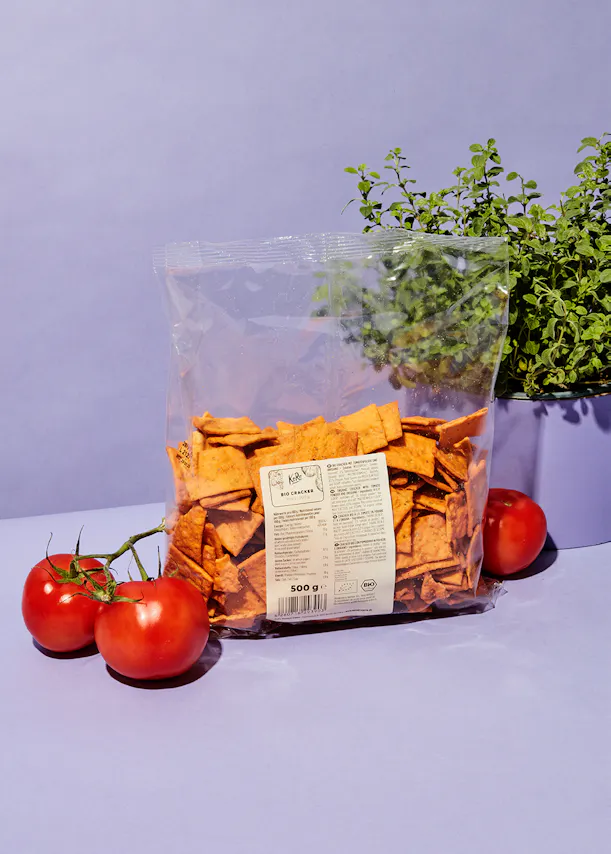a bag of tortilla chips sits next to two tomatoes and a plant