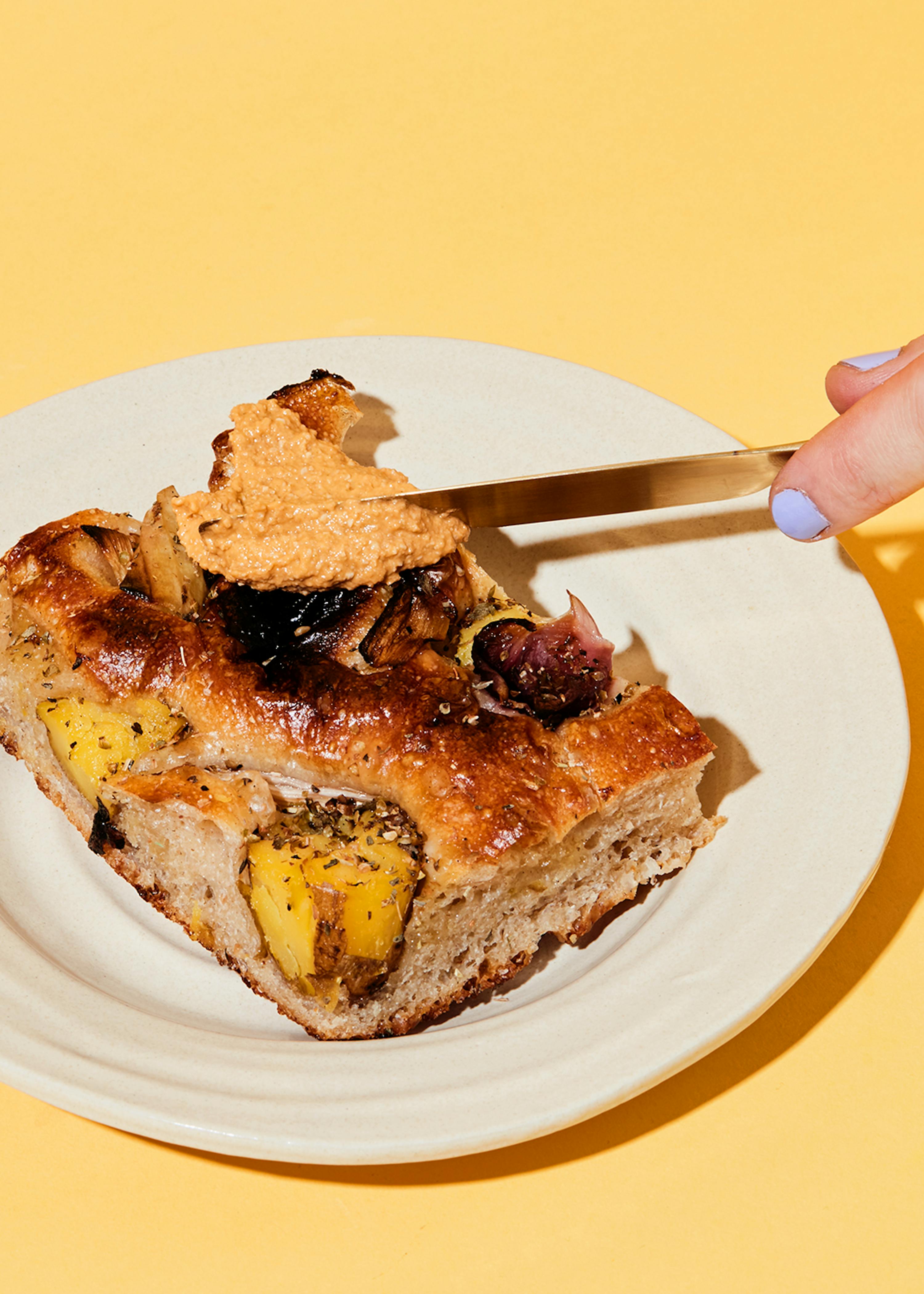 a person is spreading a sauce on a piece of bread on a white plate