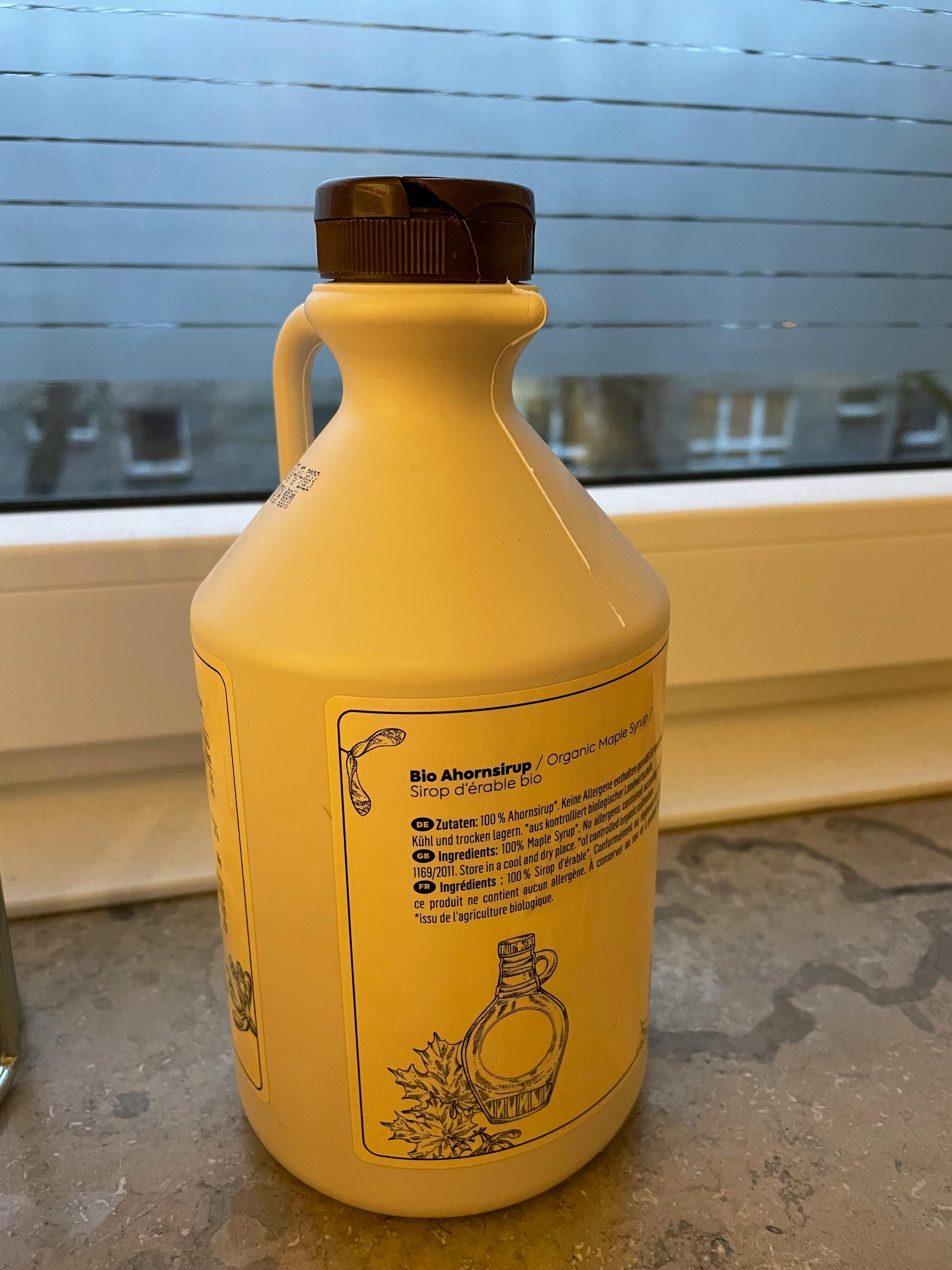 a bottle of maple syrup sits on a window sill