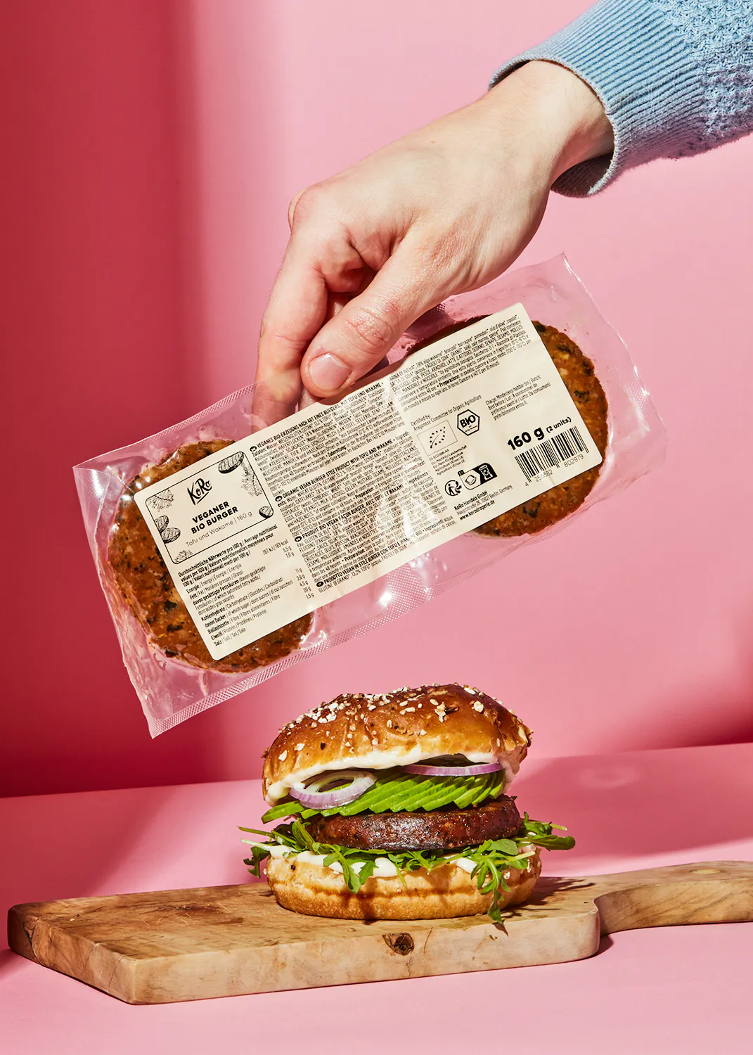 a person is holding a package of vegetable burger patties over a hamburger