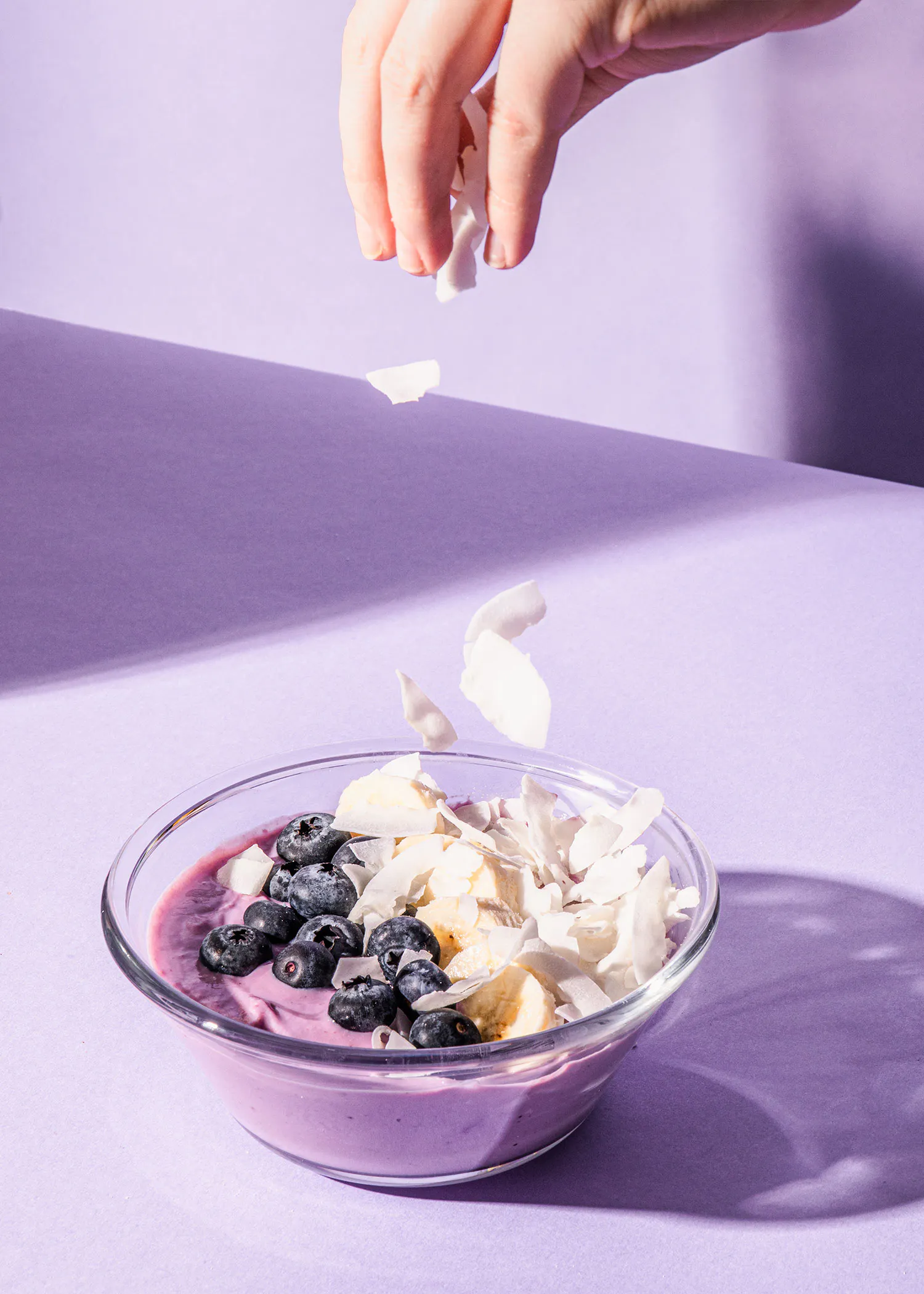 une personne verse de la noix de coco dans un bol de smoothie avec des bleuets et des bananes