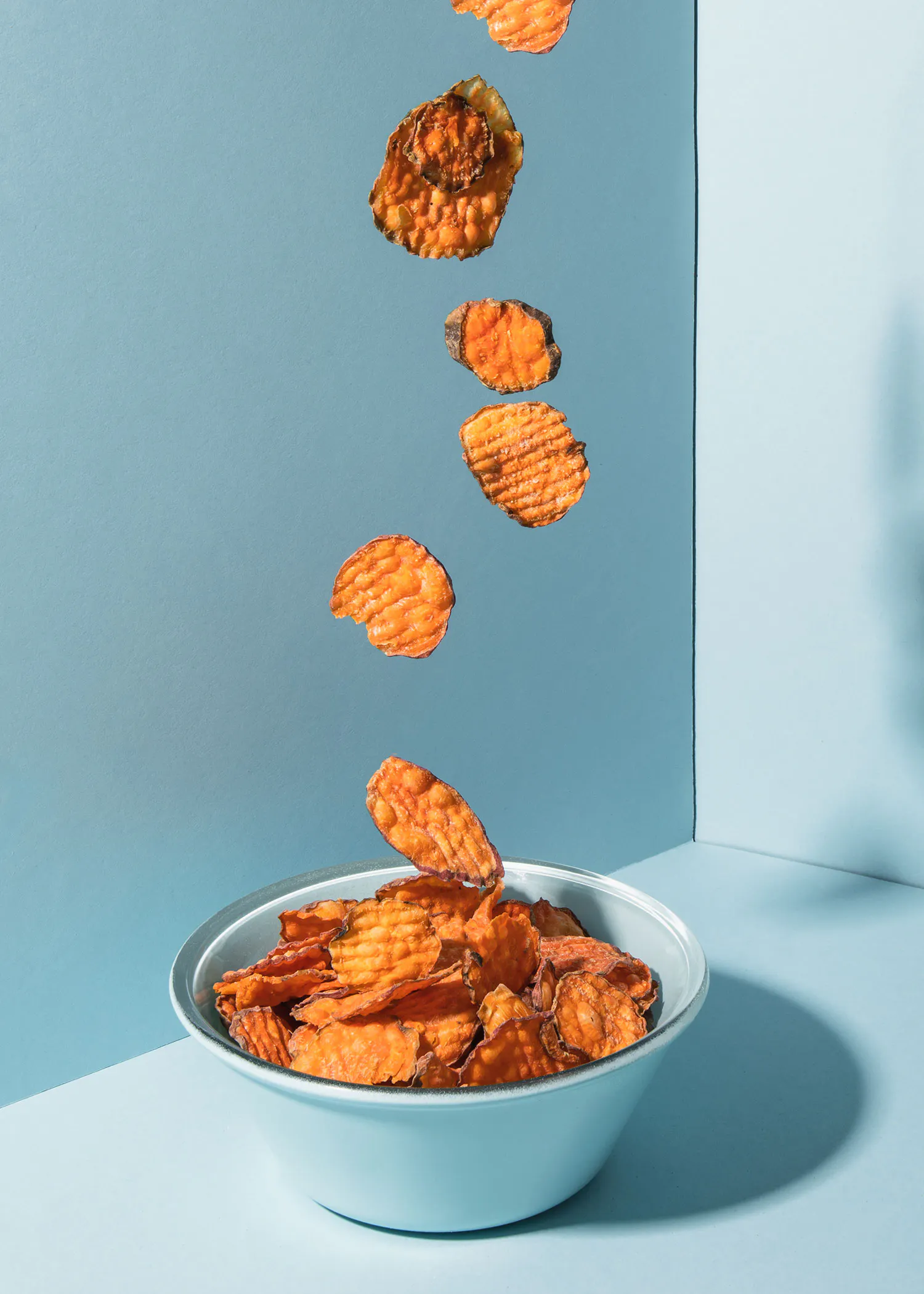 potato chips falling into a bowl on a blue surface