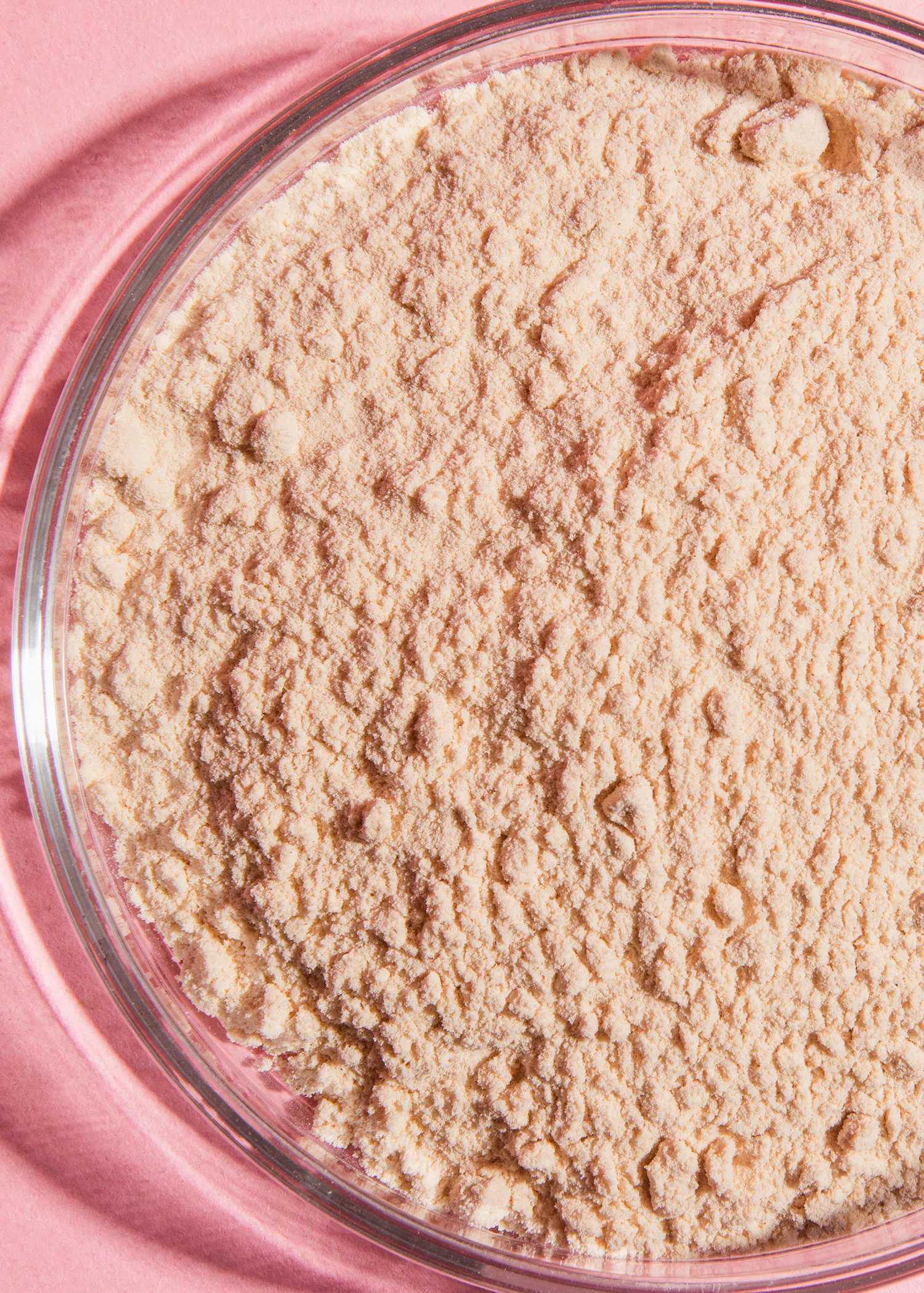 un bol en verre rempli de poudre sur fond rose