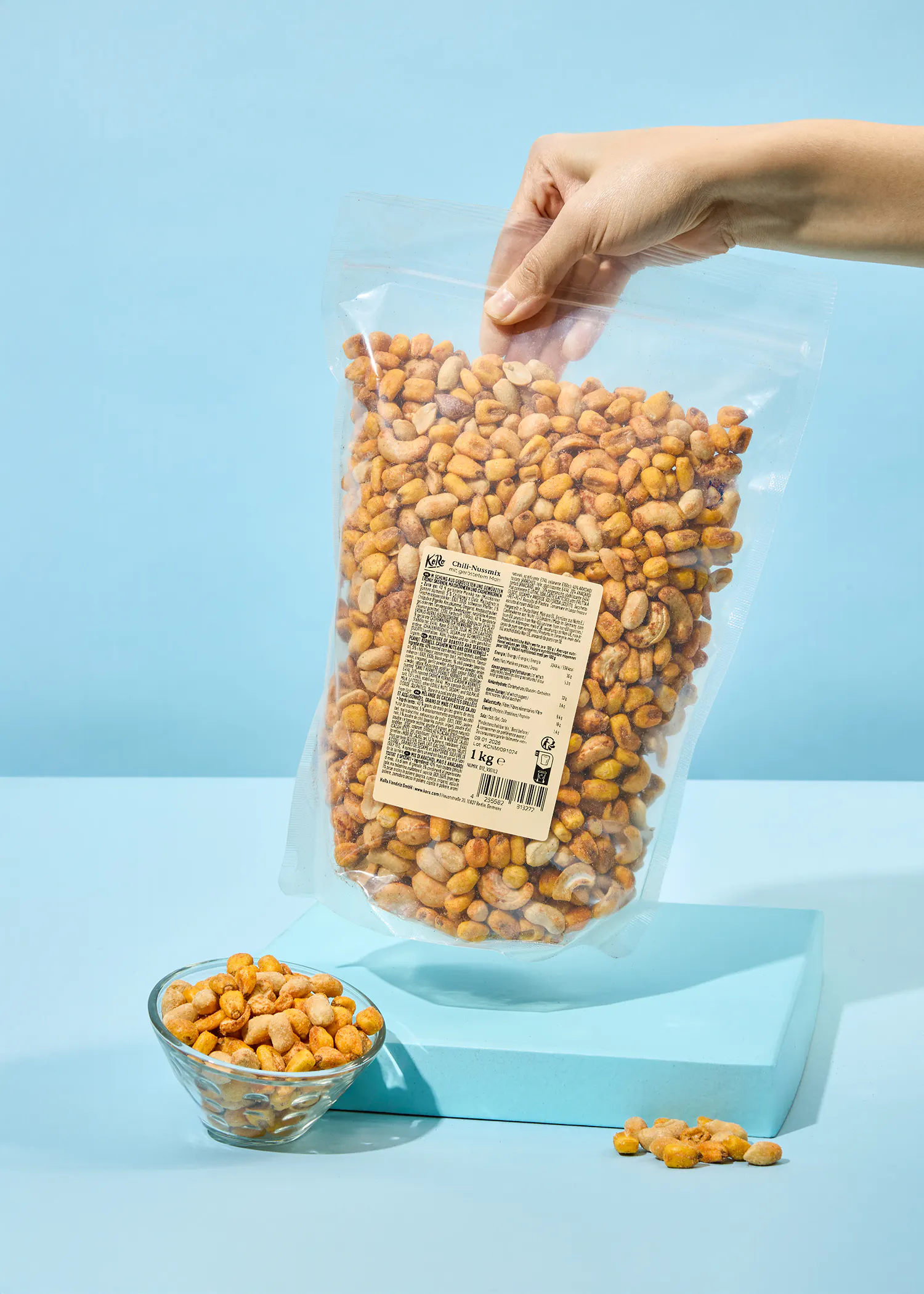 a person is holding a bag of peanuts next to a glass bowl of peanuts