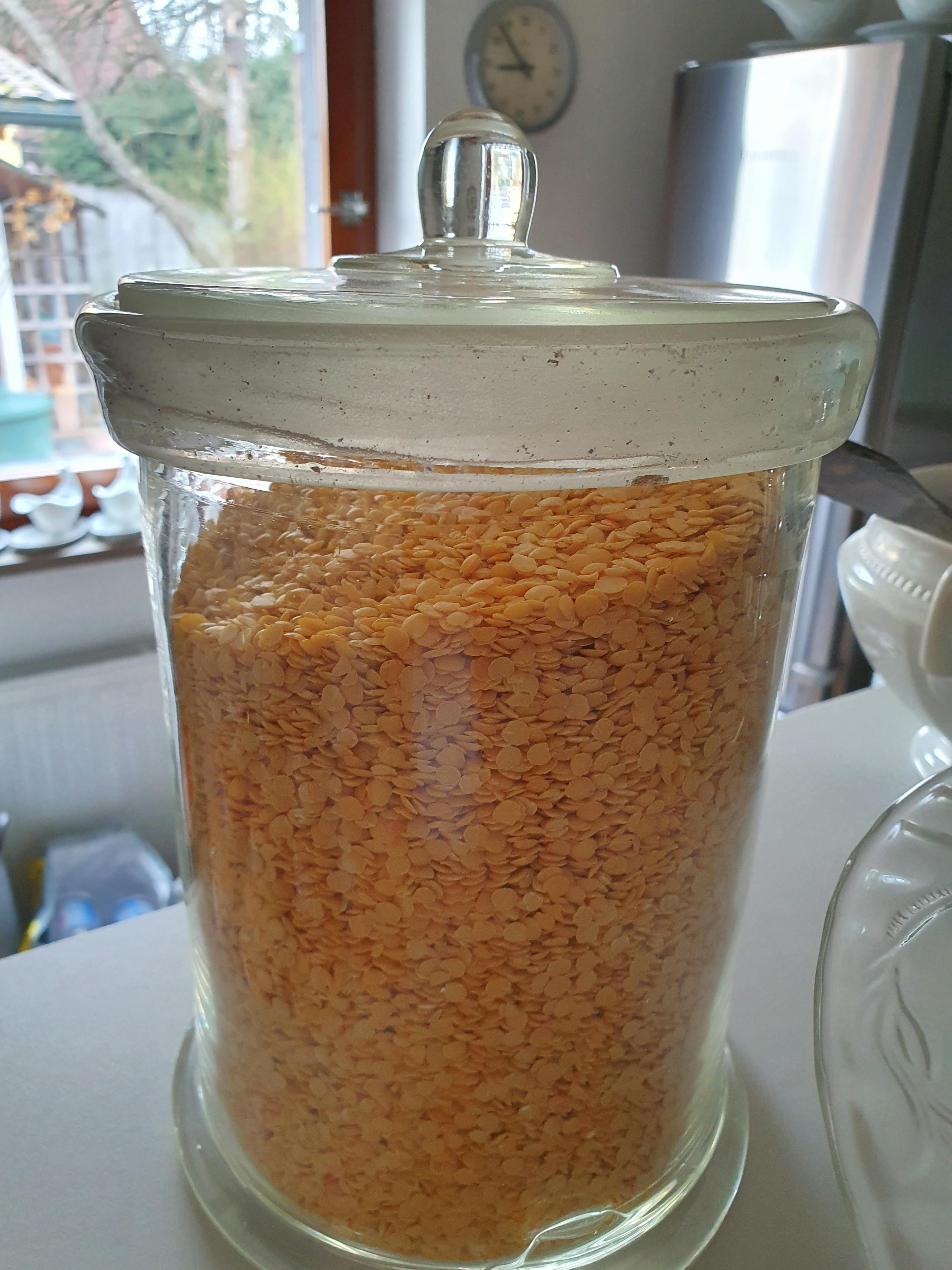 a glass jar filled with lentils sits on a counter next to a clock