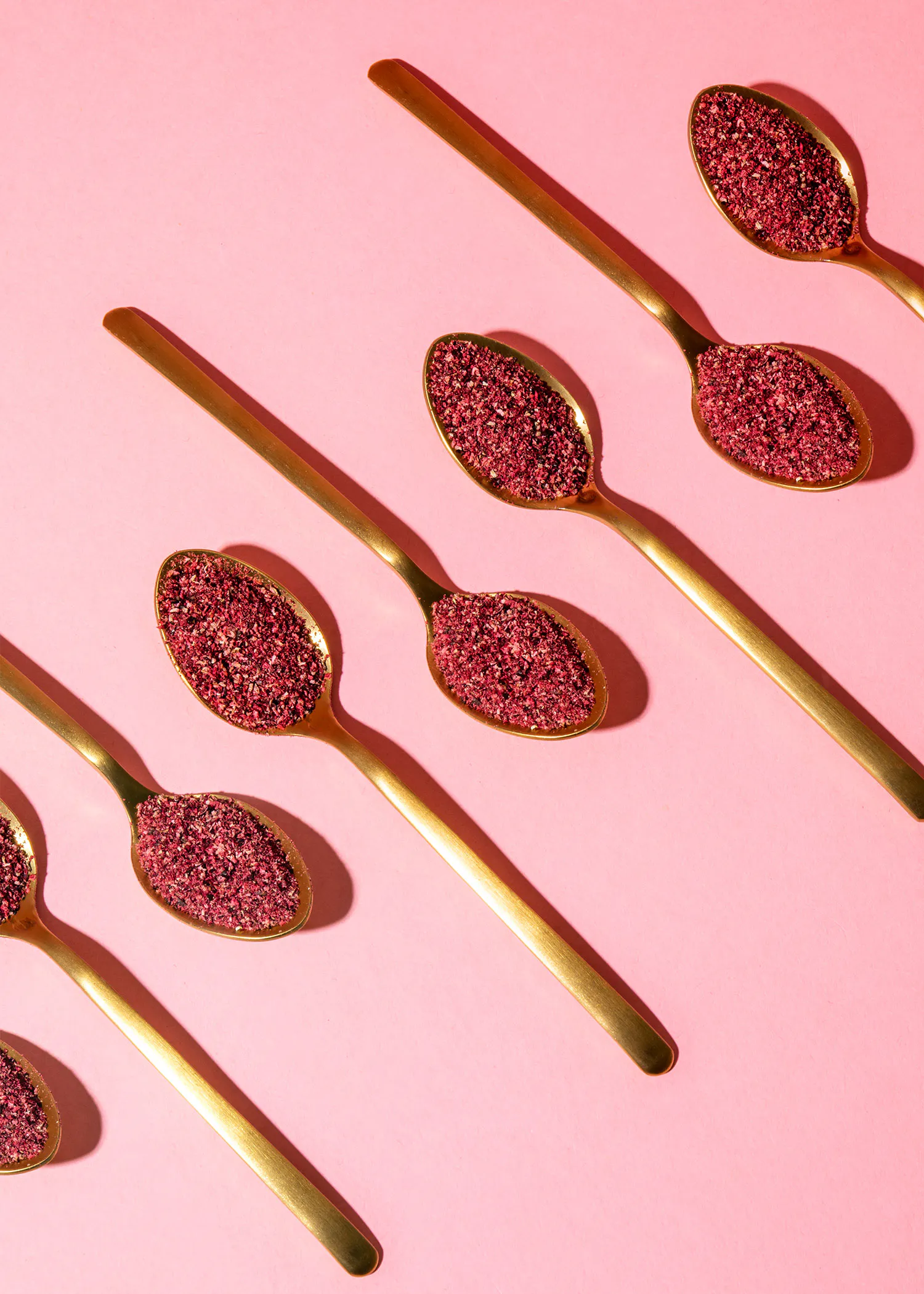 six cuillères d' or remplies de paillettes roses sur fond rose