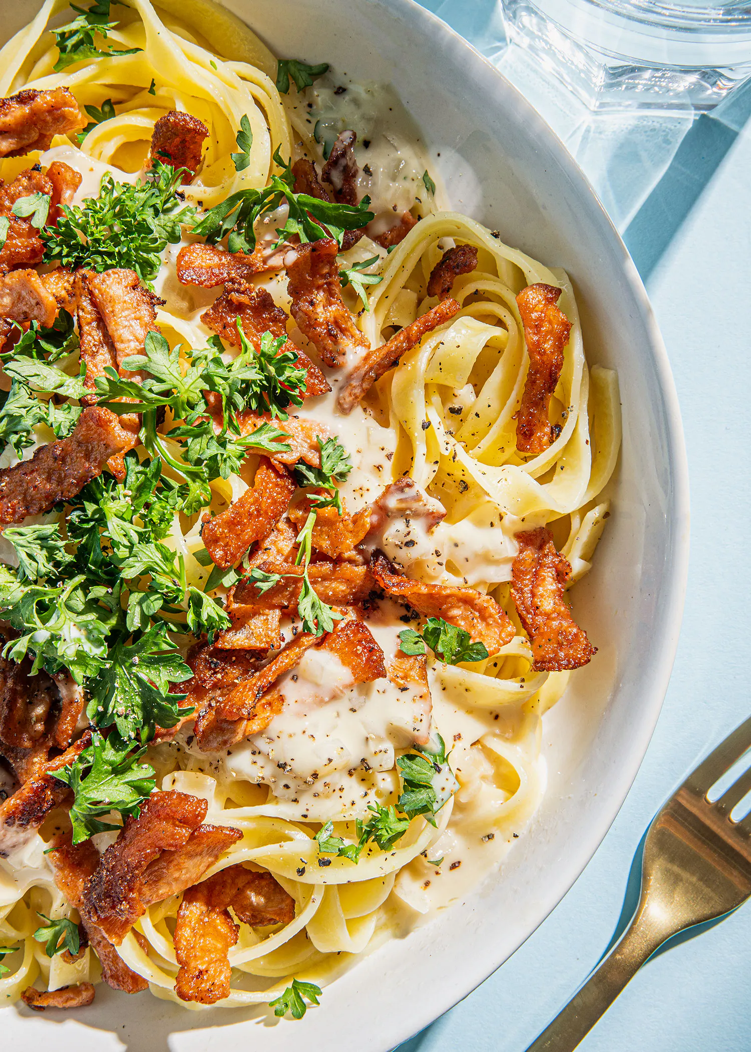 a bowl of noodles with bacon and parsley on top