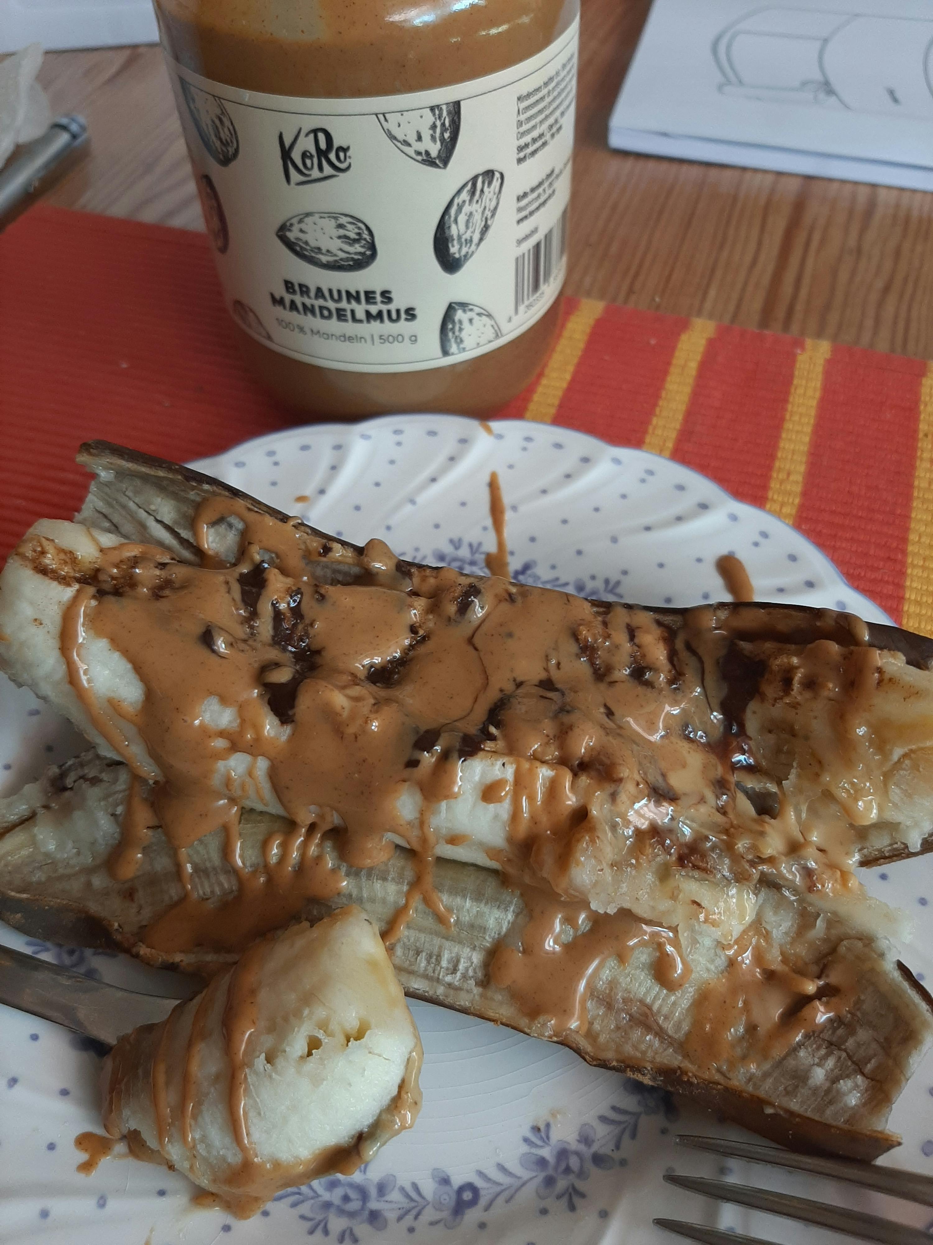 eine Banane mit Erdnussbutter auf einem weißen Teller neben einer Flasche Erdnussbutter