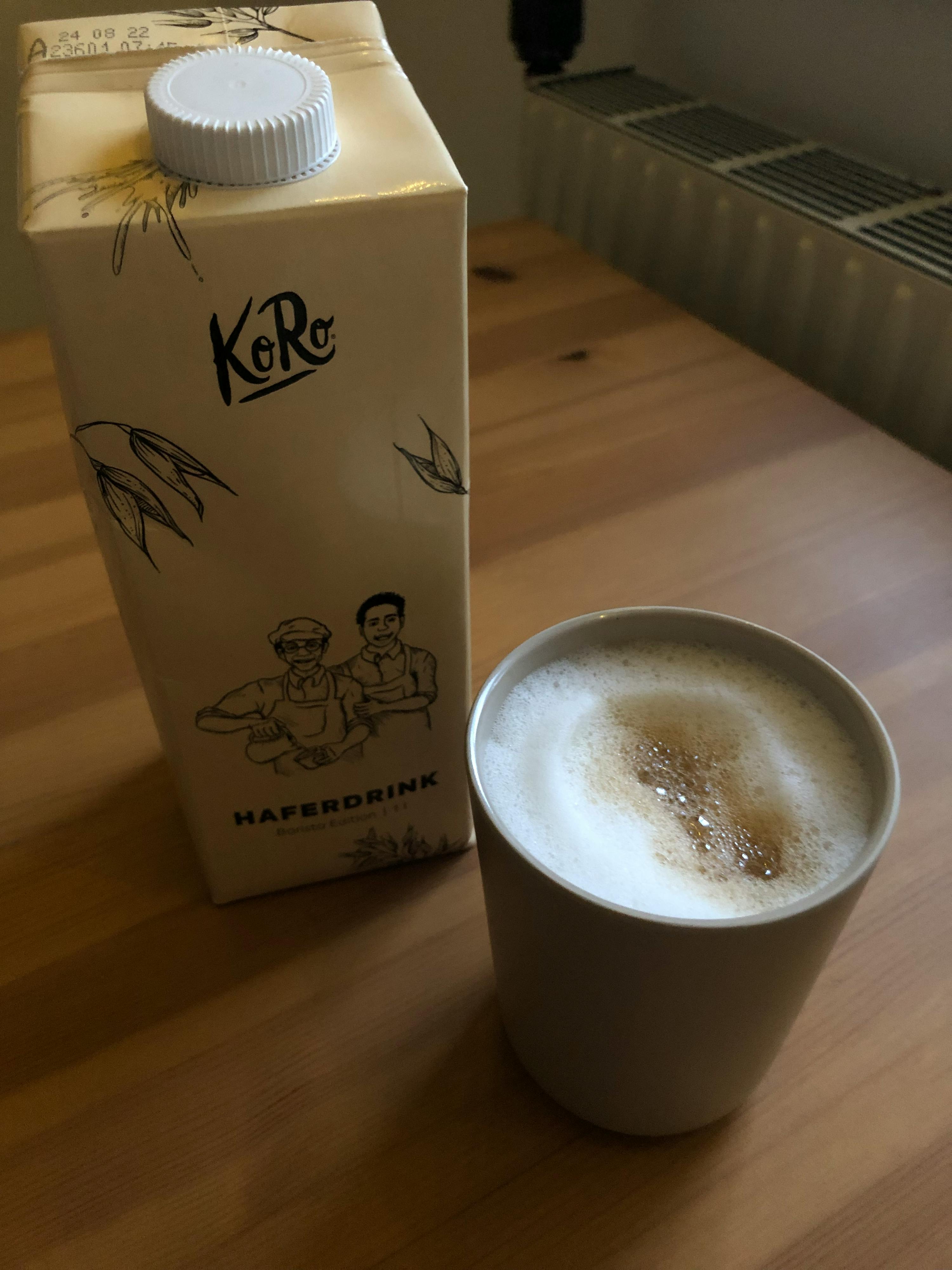 a carton of haferdrink next to a cup of coffee