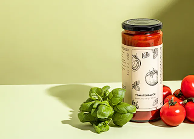 a jar of tomato sauce sits on a table next to tomatoes and basil