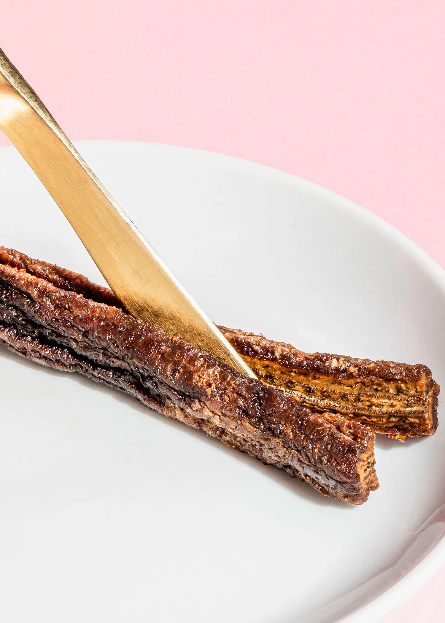 une assiette blanche avec deux bâtonnets de viande et une cuillère dorée