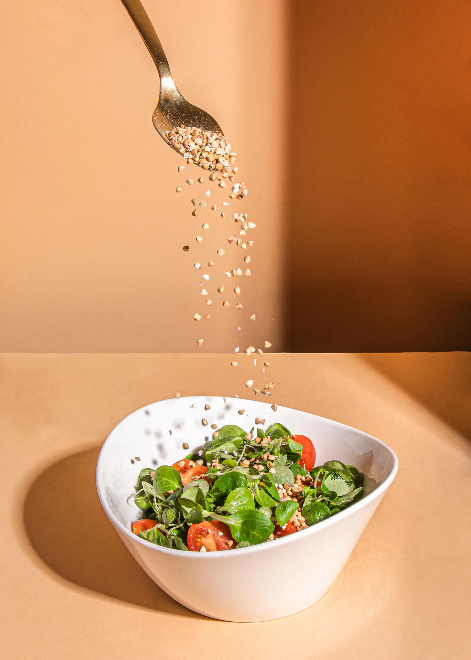 une cuillère verse des graines sur une salade