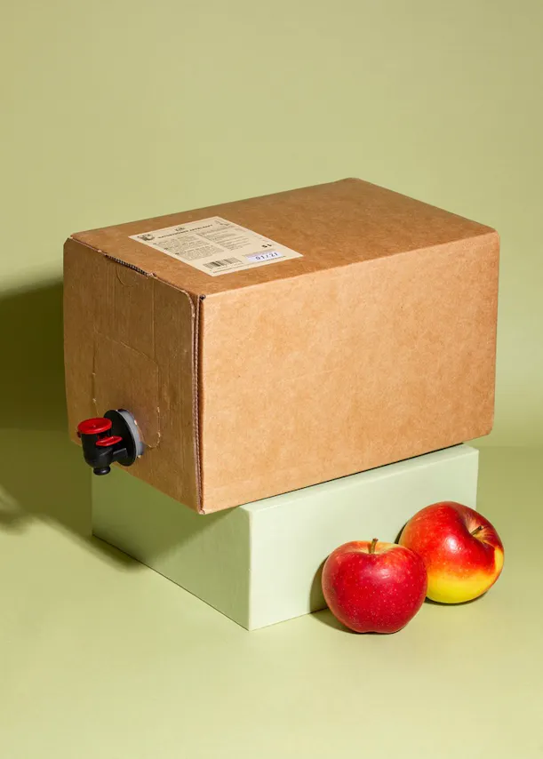 a cardboard box with a tap on it sits on a green block next to two apples