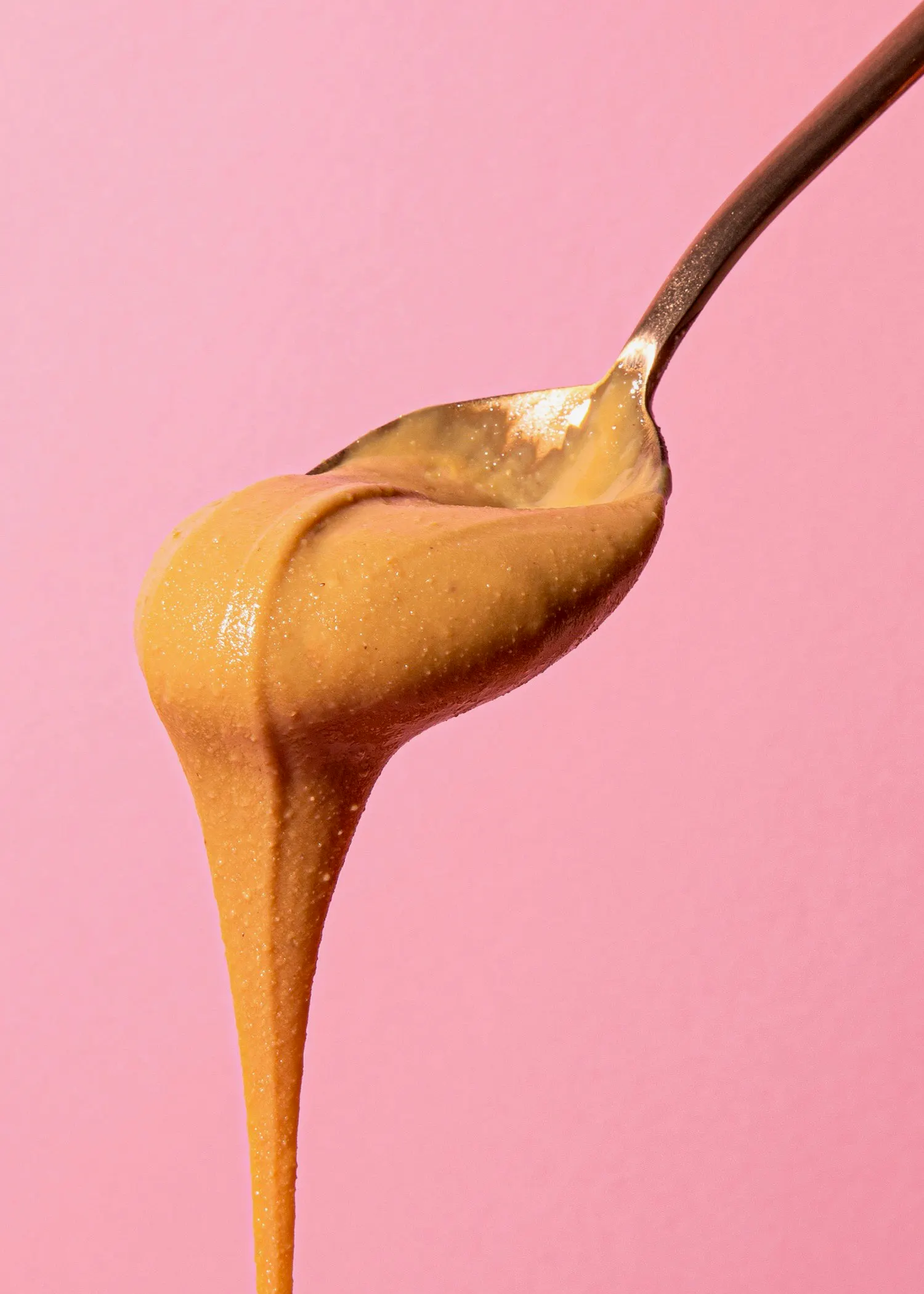 Erdnussbutter wird aus einem Löffel auf einem rosa Hintergrund gegossen