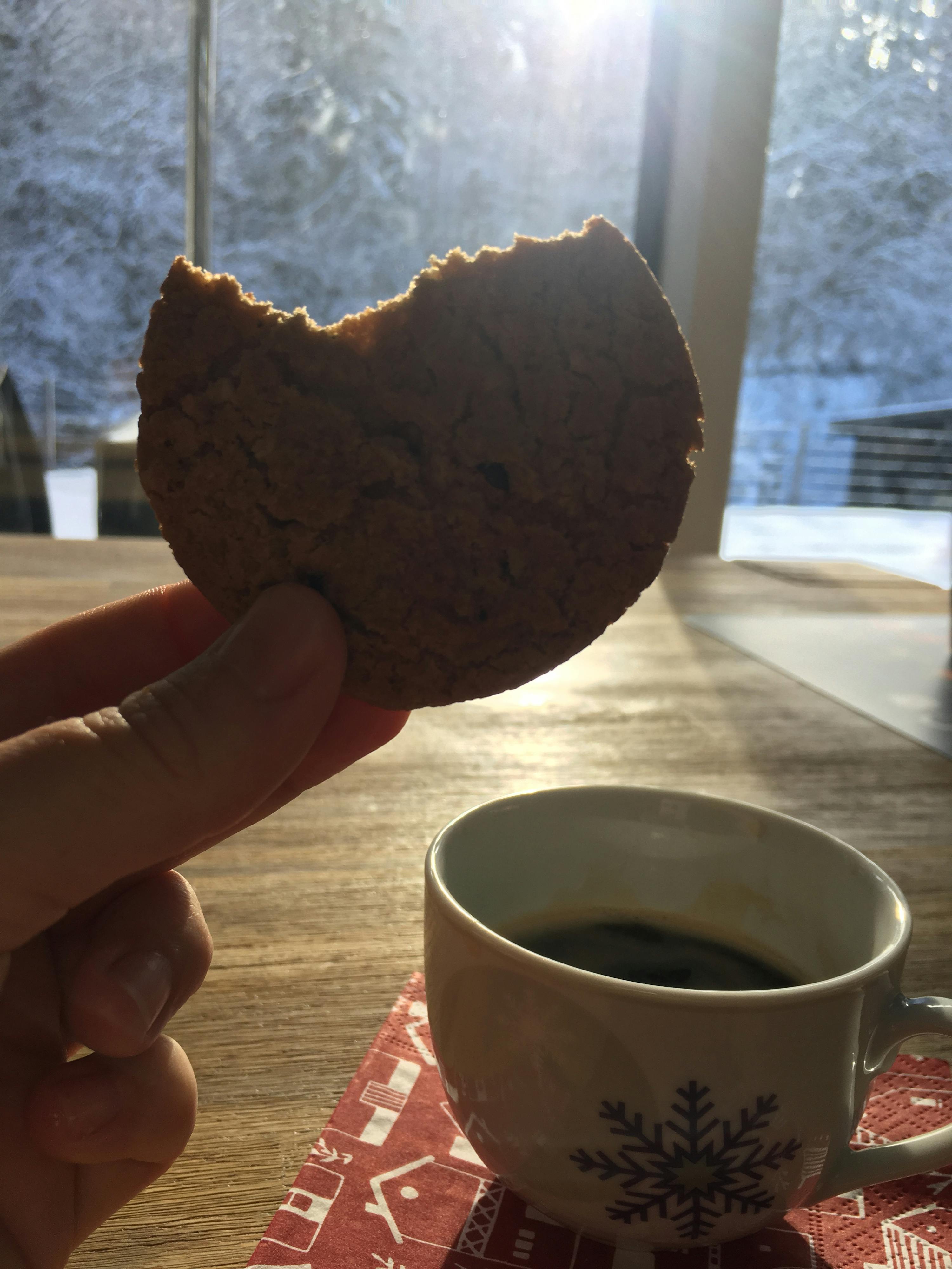 une personne tient un biscuit à côté d' une tasse de café avec un flocon de neige