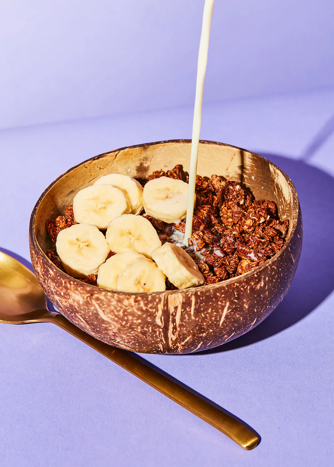 un bol de céréales avec des bananes et du lait est versé avec une cuillère