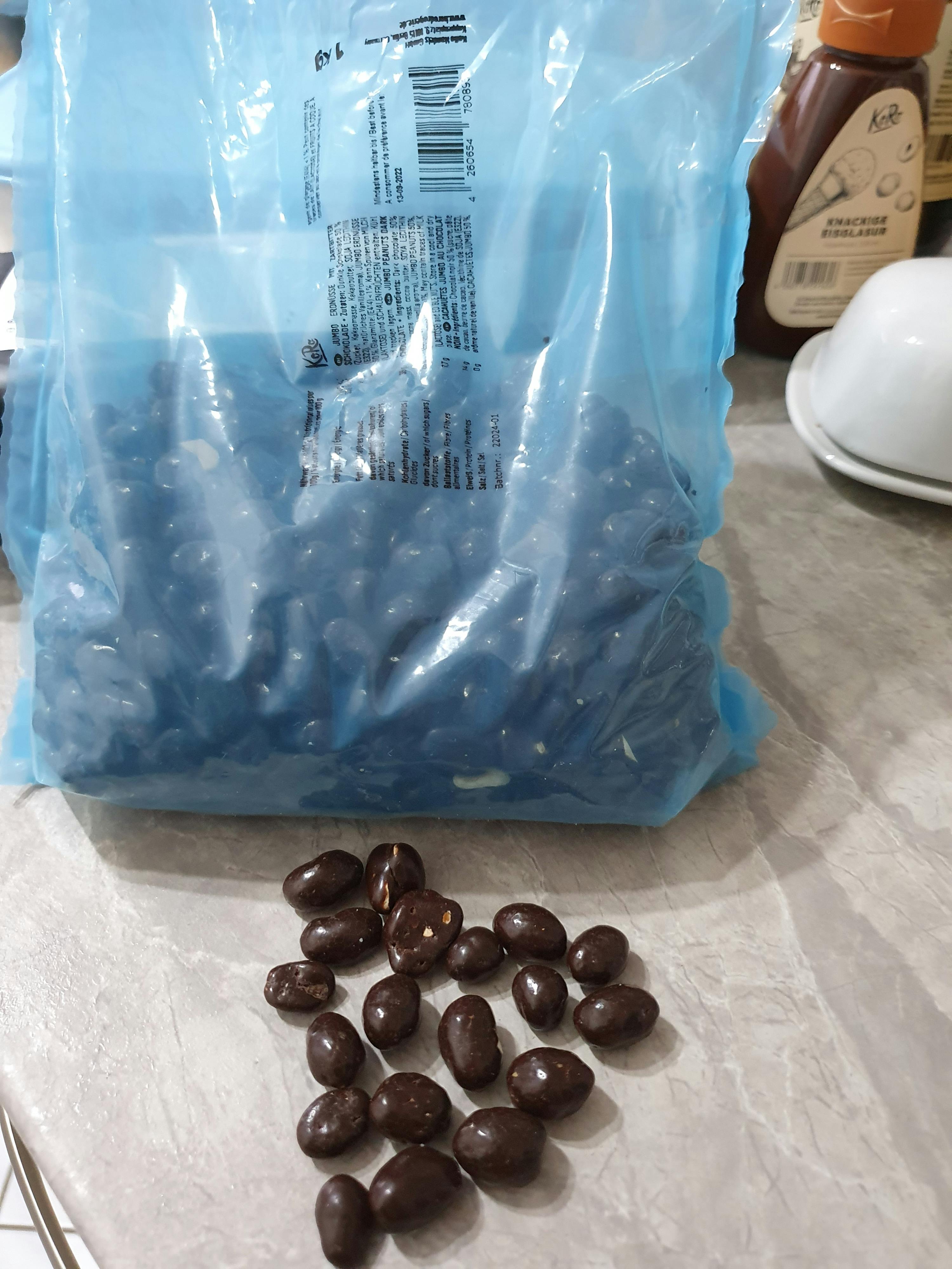 eine blaue Plastiktüte voller Schokoladenbeeren neben einem Haufen Schokoladenbeeren