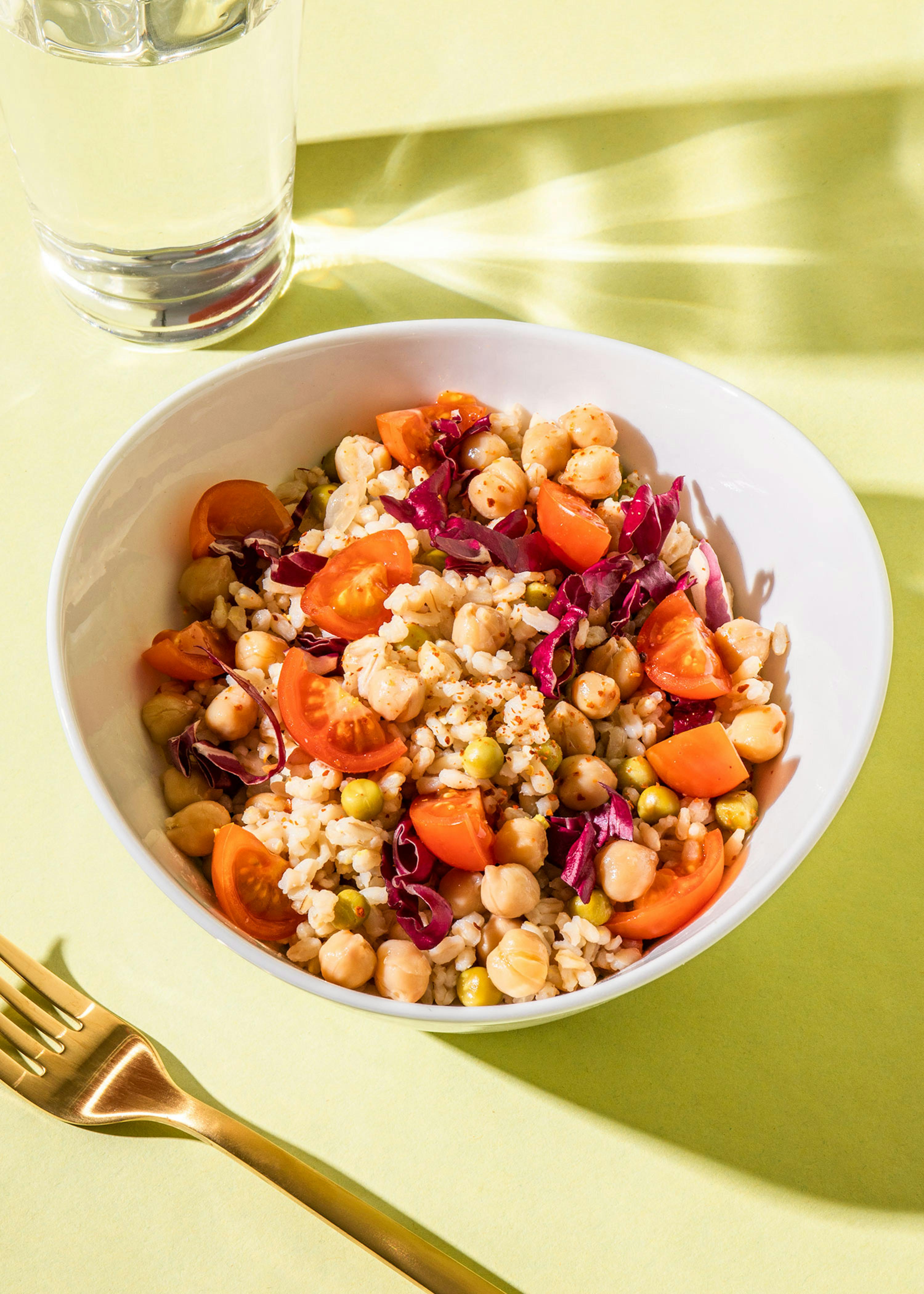 a bowl of food with chickpeas tomatoes and red cabbage next to a glass of water