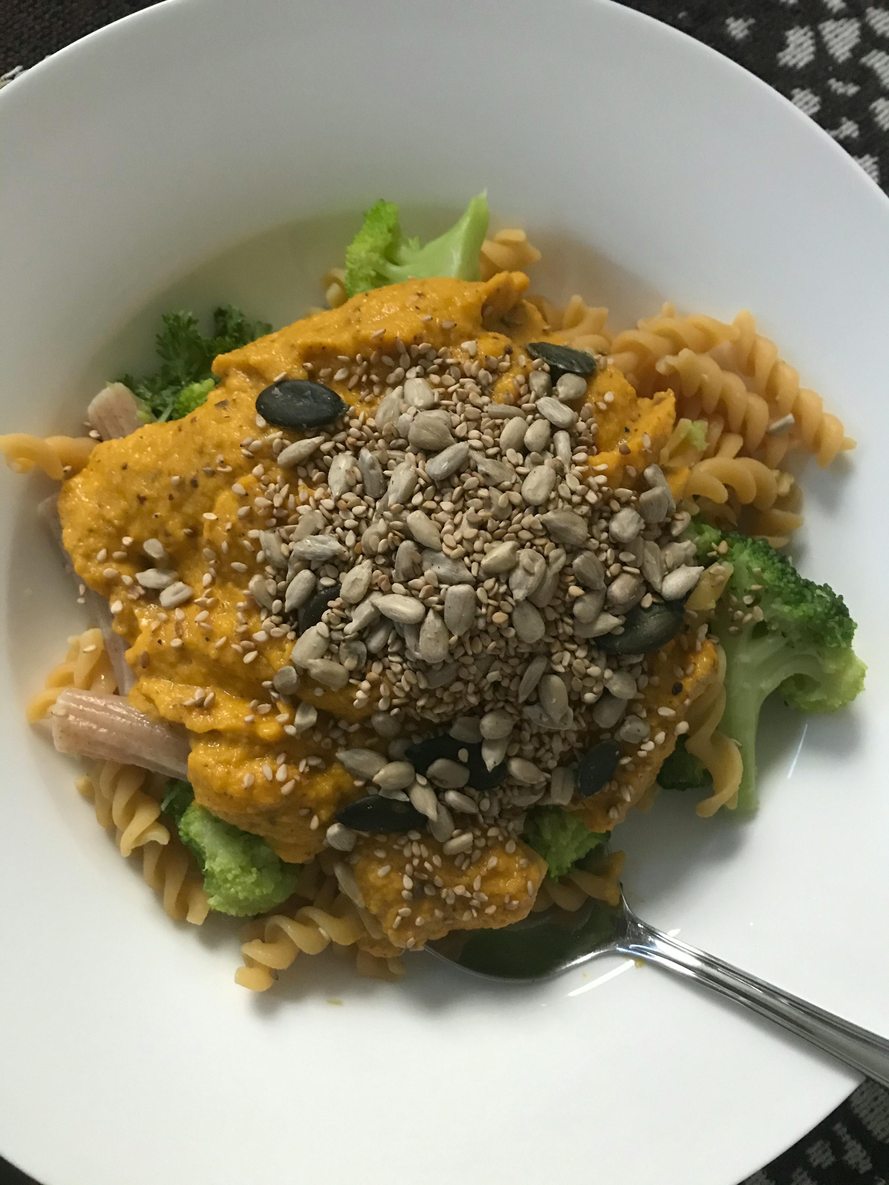 a white plate topped with pasta broccoli and sunflower seeds
