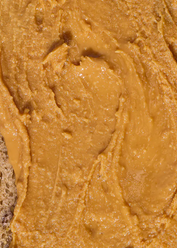 gros plan sur du beurre de cacahuète crémeux et texturé étalé sur une tranche de pain.