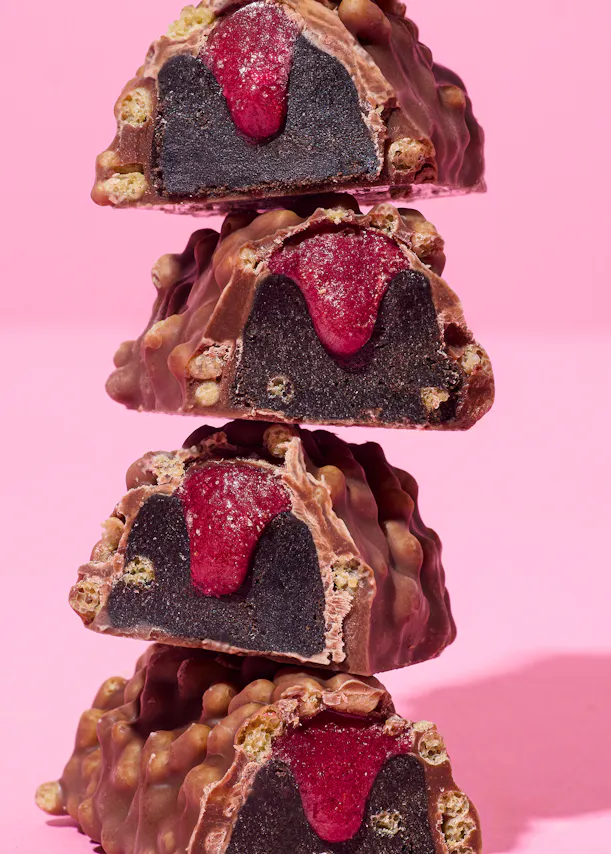 four pieces of chocolate with a raspberry filling are stacked on top of each other on a pink background