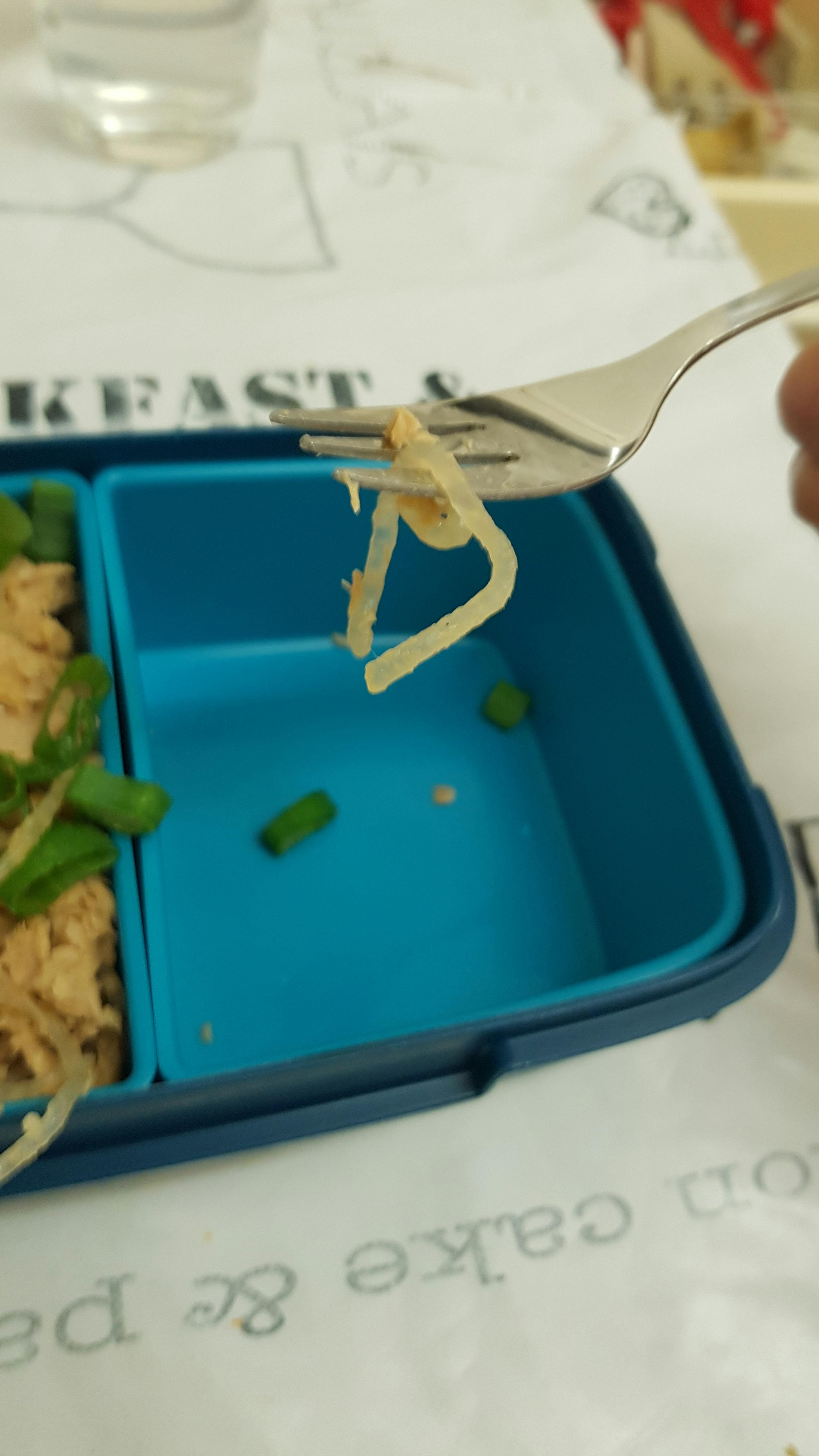 eine Person hält einen Löffel über einem blauen Lunchcontainer