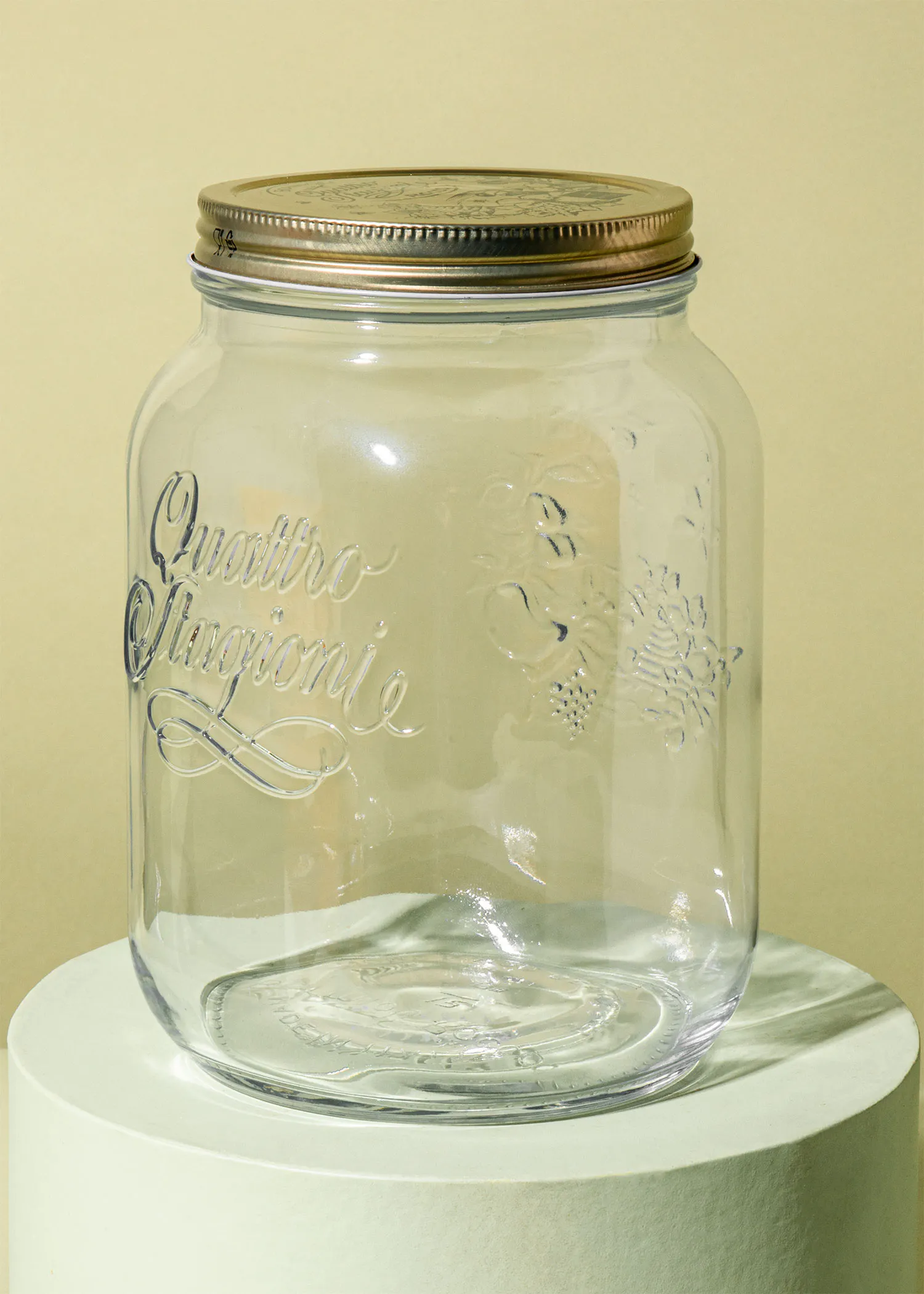 ein Glasgefäß mit einem goldenen Deckel steht auf einem weißen Sockel