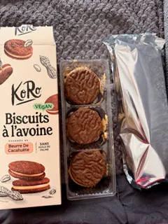una confezione aperta di biscotti all'avena koro ripieni di burro di arachidi con tre biscotti disposti in un vassoio di plastica trasparente sopra la scatola di cartone.