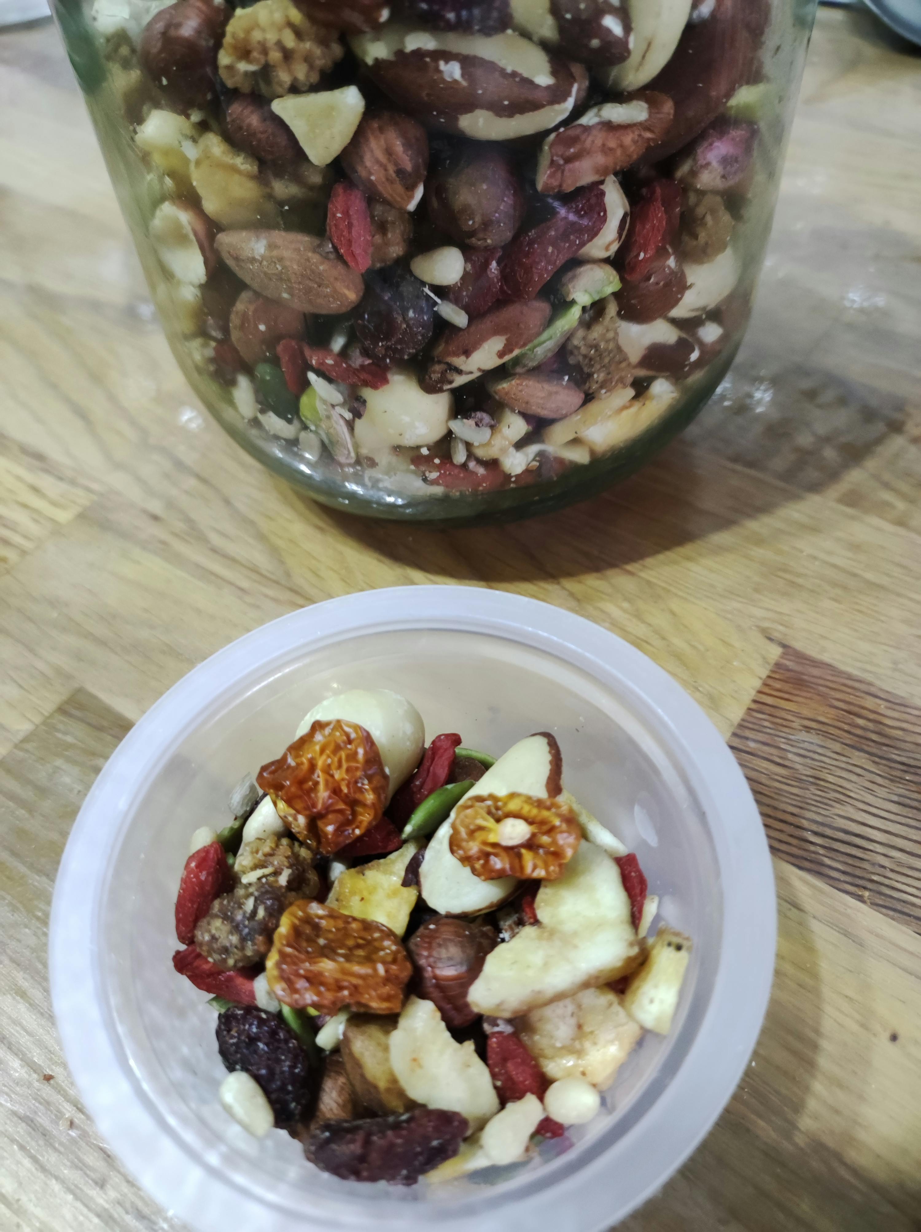 eine Schüssel mit Nüssen und Früchten neben einem Glas voller Nüsse