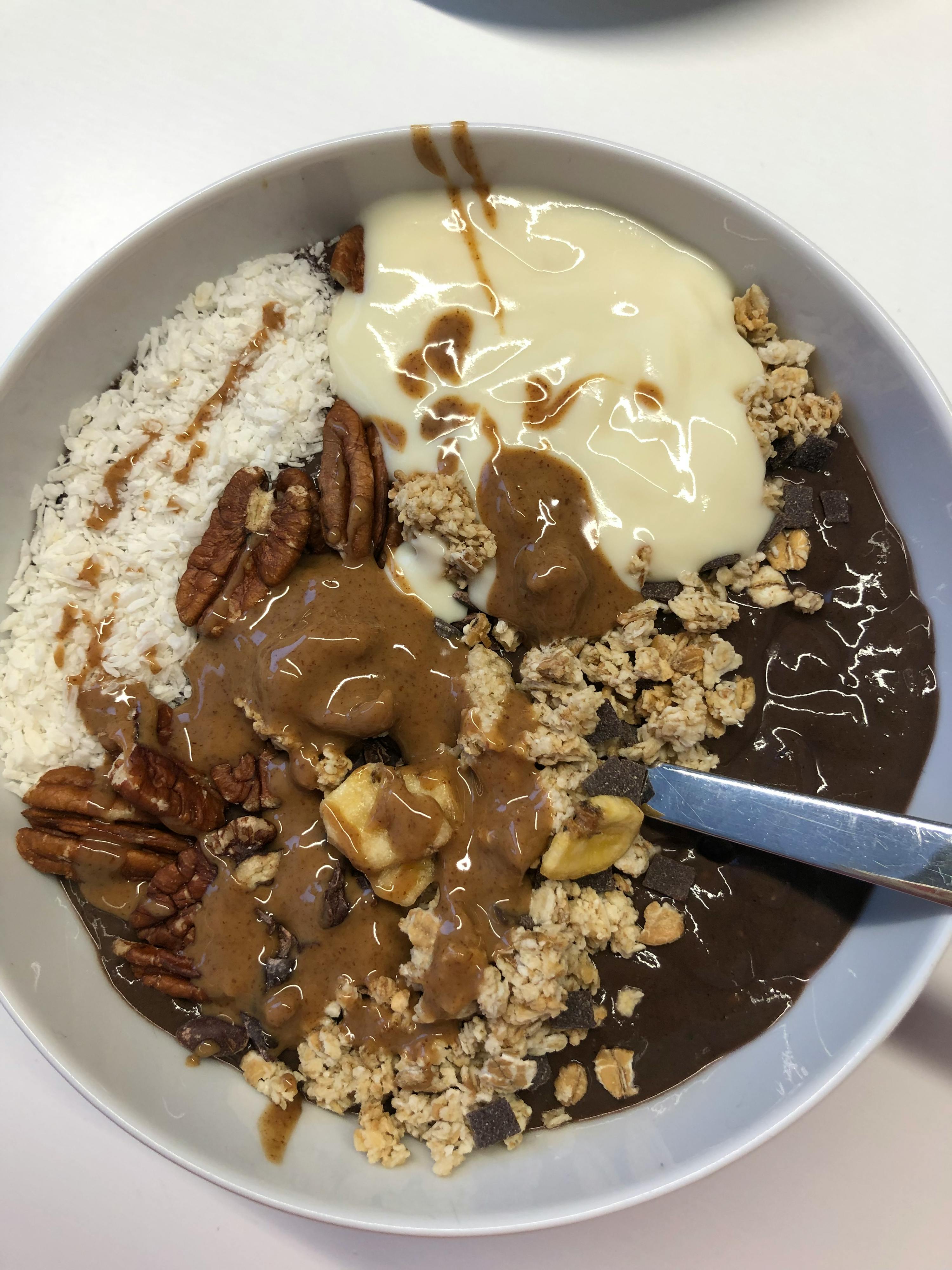 a bowl of food with a spoon in it including yogurt pecans and granola