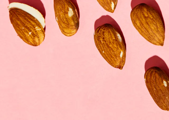 un tas d' amandes sur fond rose avec une amande coupée en deux