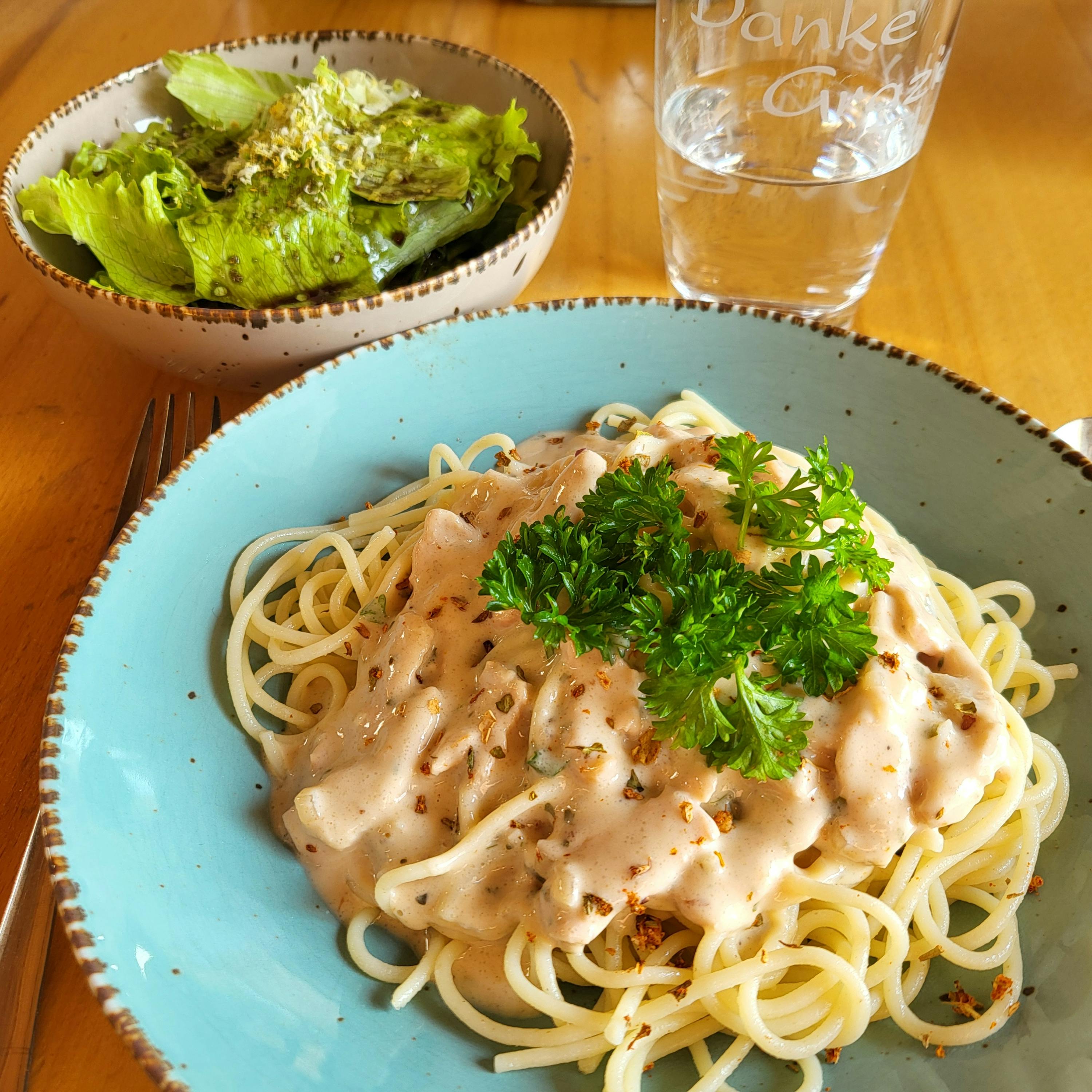 ein blauer Teller mit Nudeln und einer Schüssel Salat neben einem danke-glas