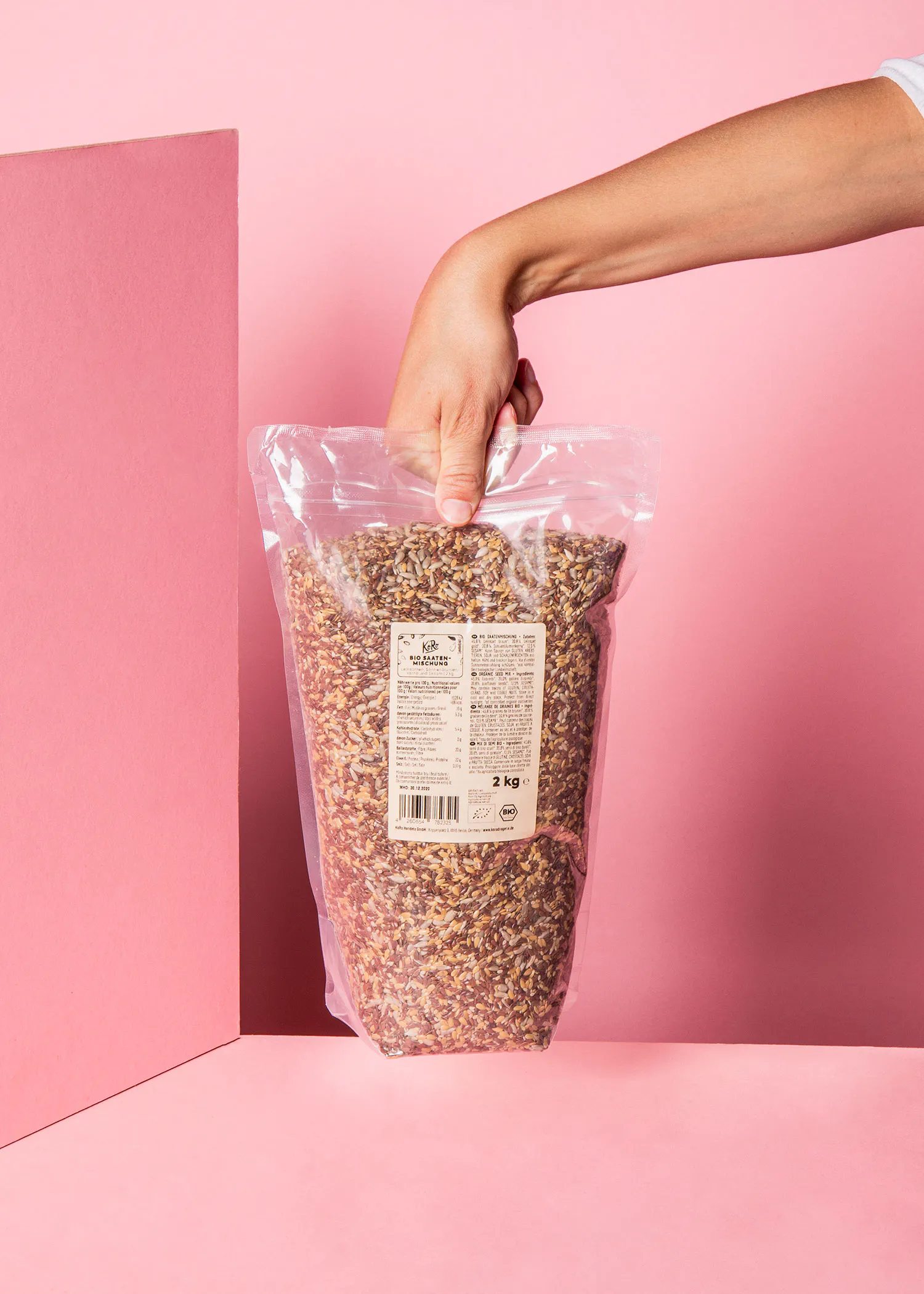 une personne tient un sac en plastique rempli de graines sur fond rose