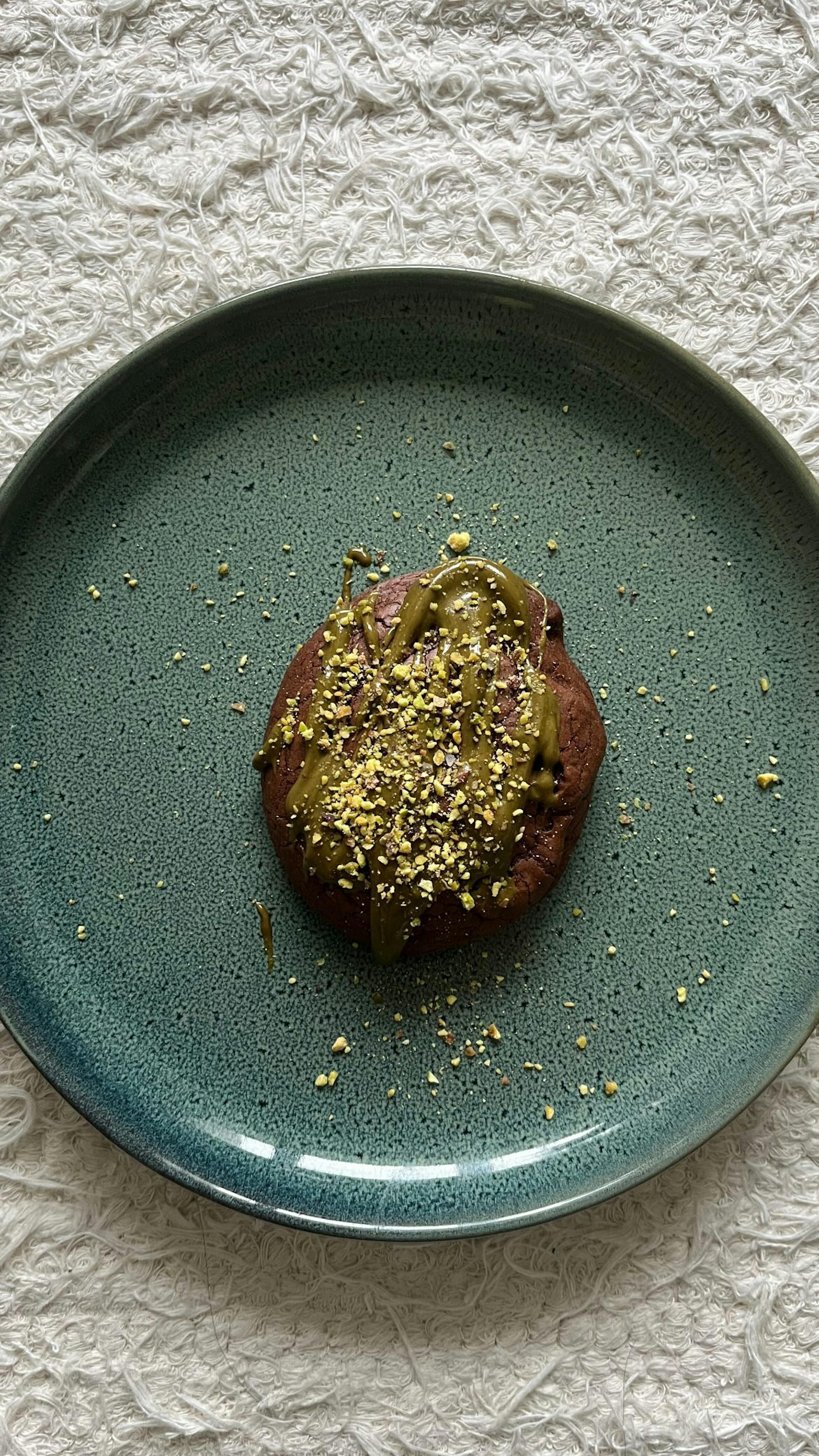 une assiette en céramique bleue avec un biscuit au chocolat avec du beurre de pistache sur le dessus