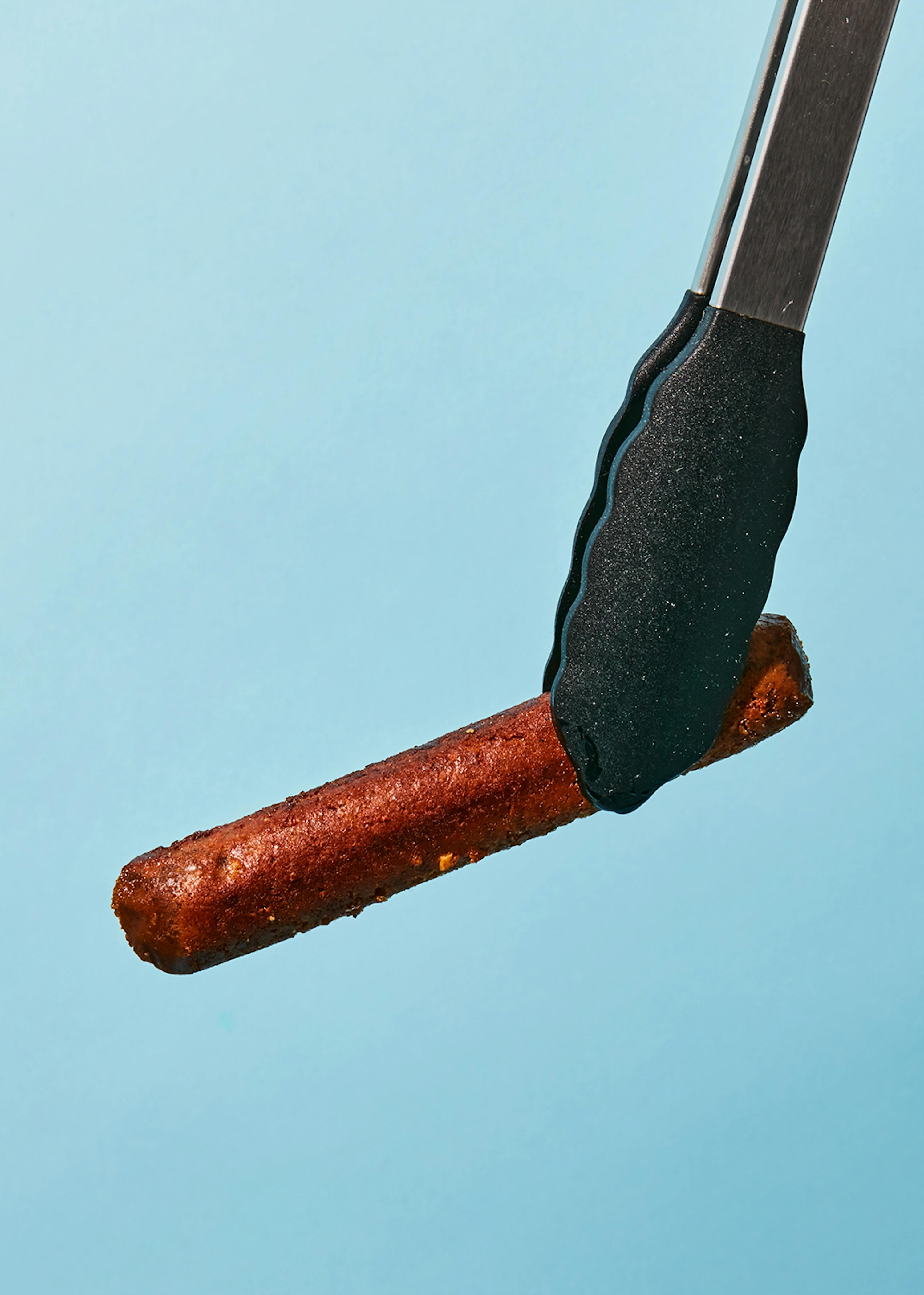 eine zange hält einen bratwurst auf blauem hintergrund
